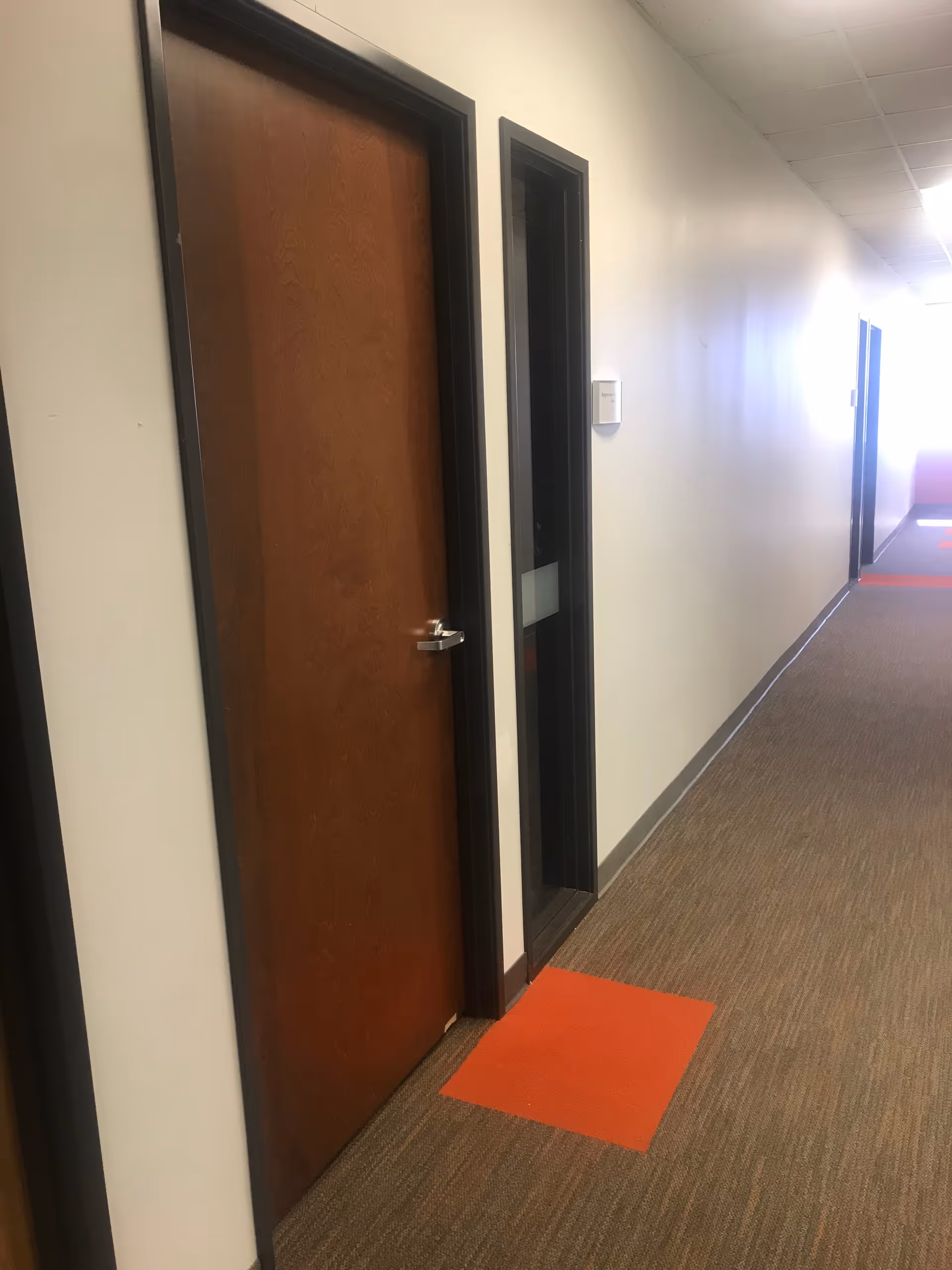 Narrow interior hallway in a senior living facility with closed wooden doors and orange floor marker.