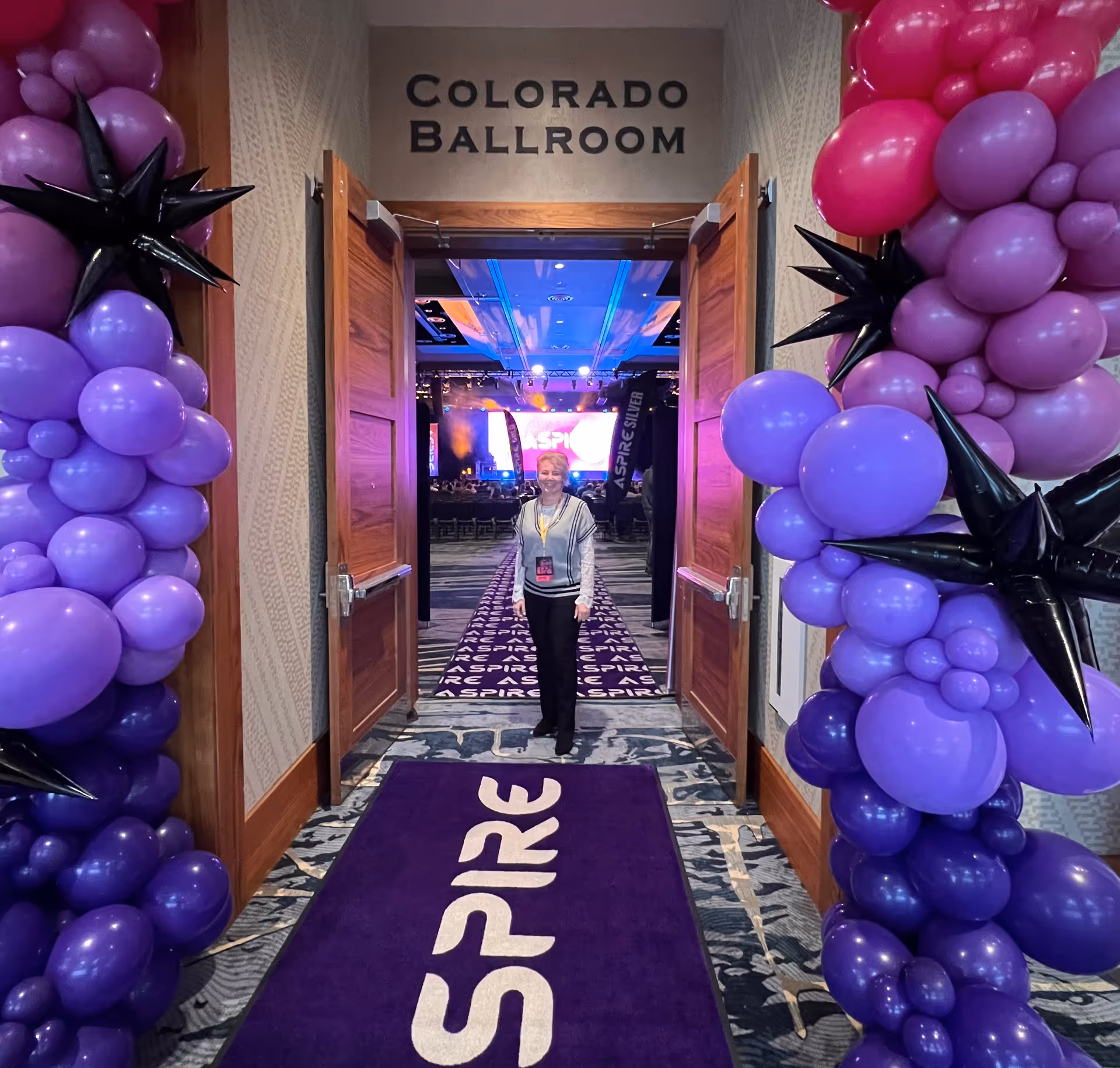 Person stands in a decorated interior corridor with purple balloon arches and Colorado Ballroom sign.