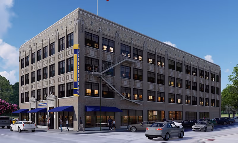 Four-story brick building with blue awnings, street-level entrances, cars parked and people walking in front.
