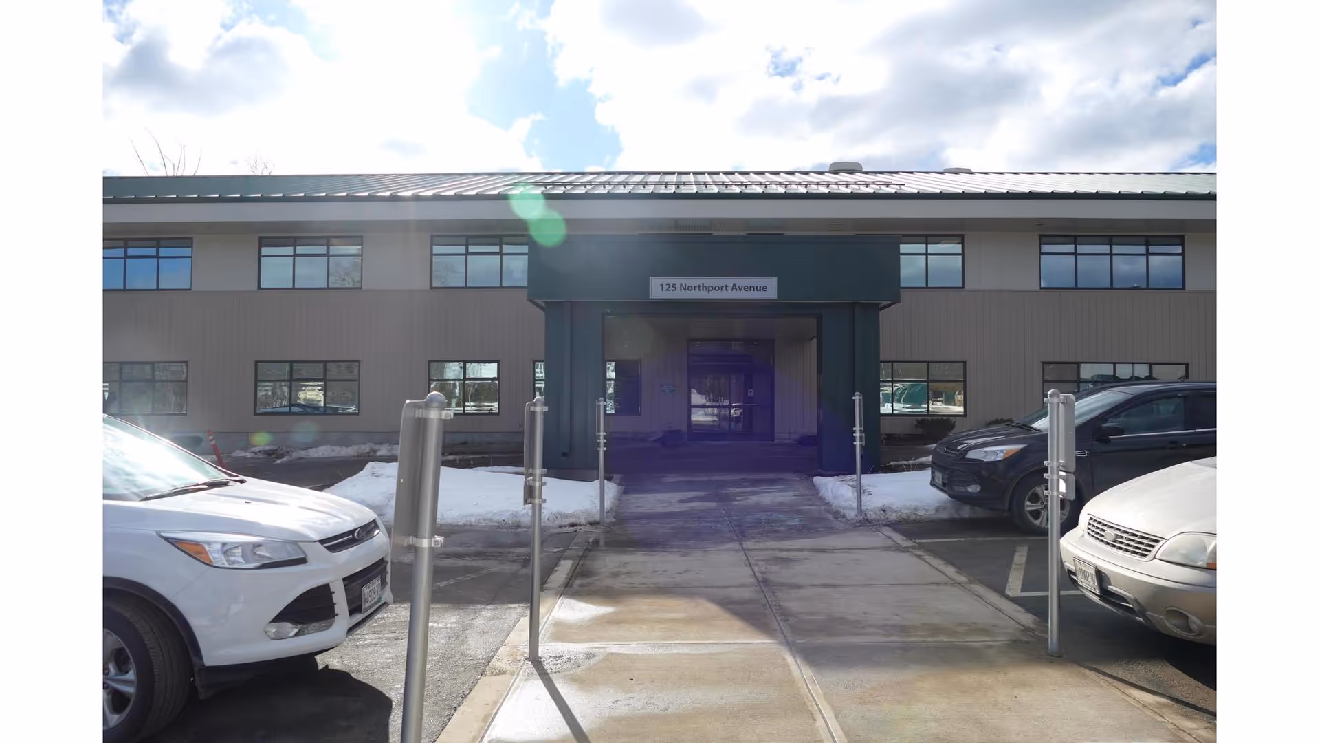 Exterior view of a modern healthcare facility entrance with parked cars.