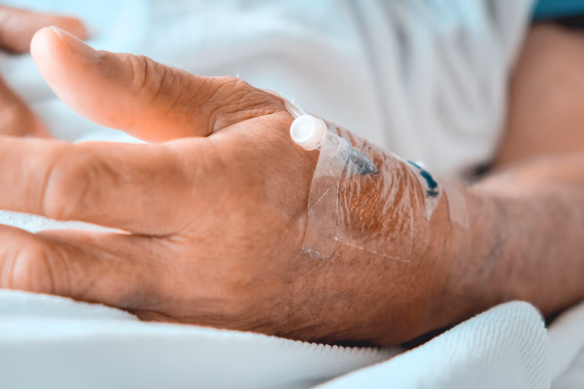 Close-up of an elderly hand with an IV cannula taped to the arm.