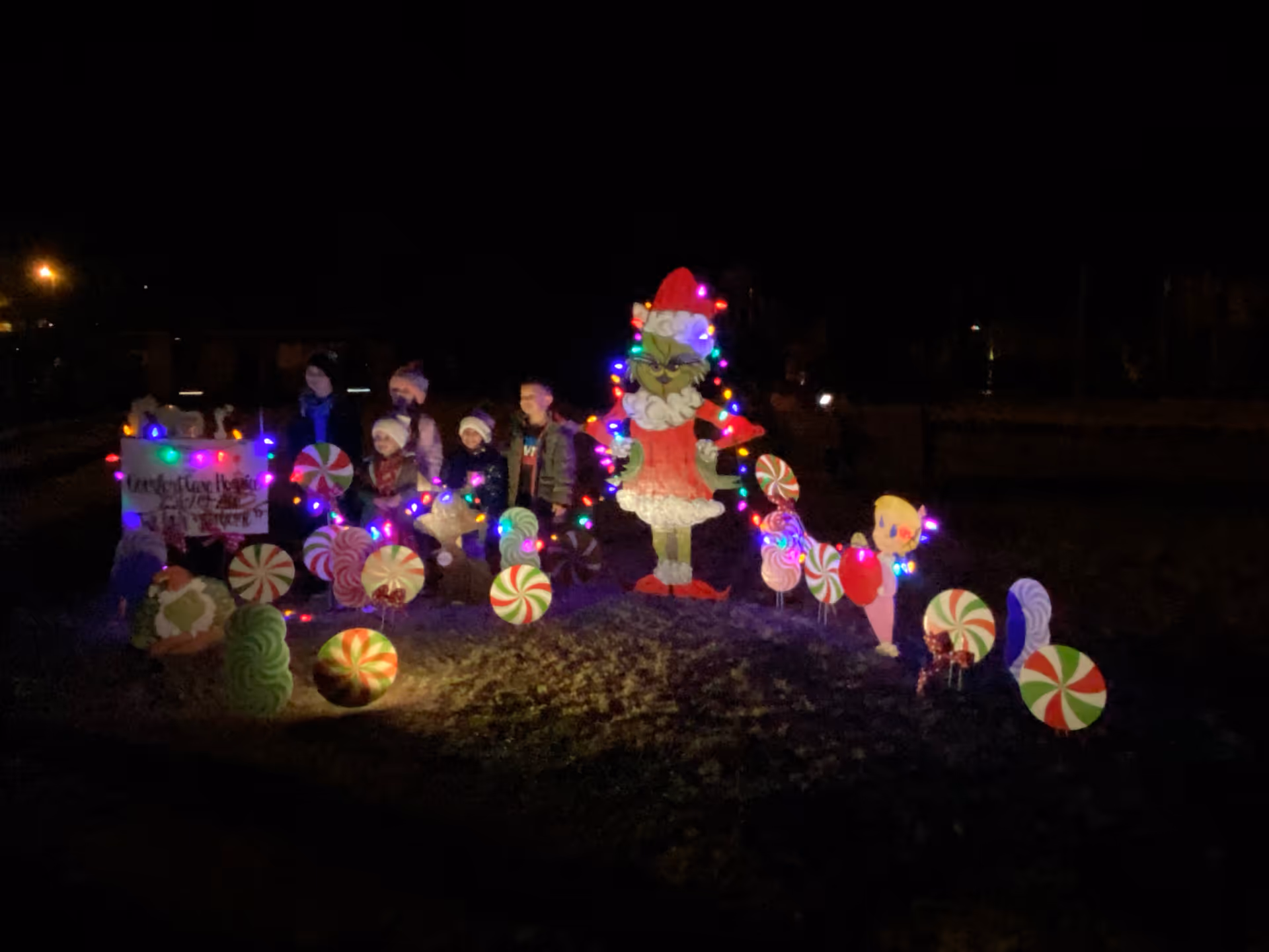 Night scene of an outdoor holiday display with illuminated figures and candy decorations.