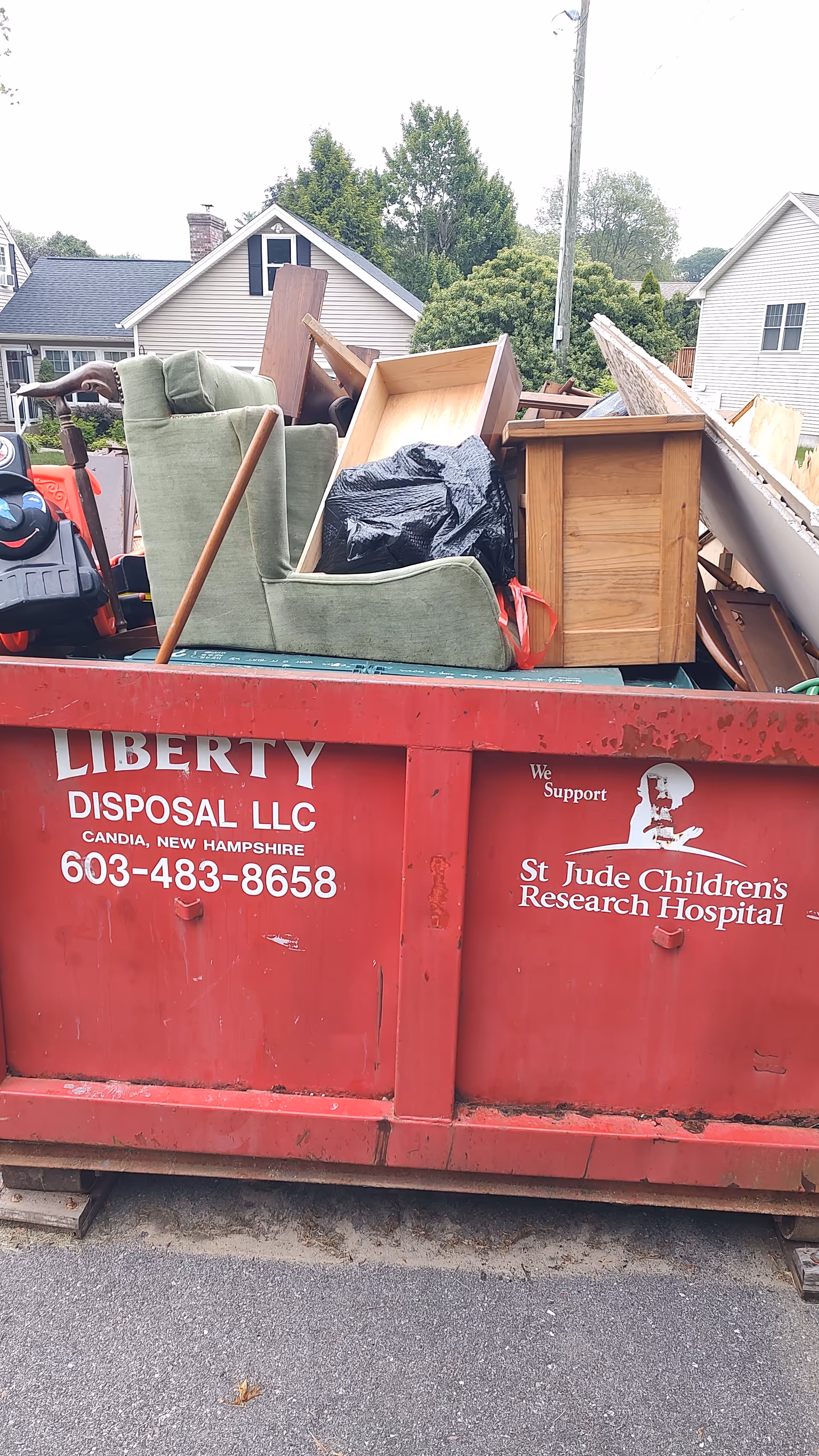 Red dumpster overflowing with discarded furniture in a residential street