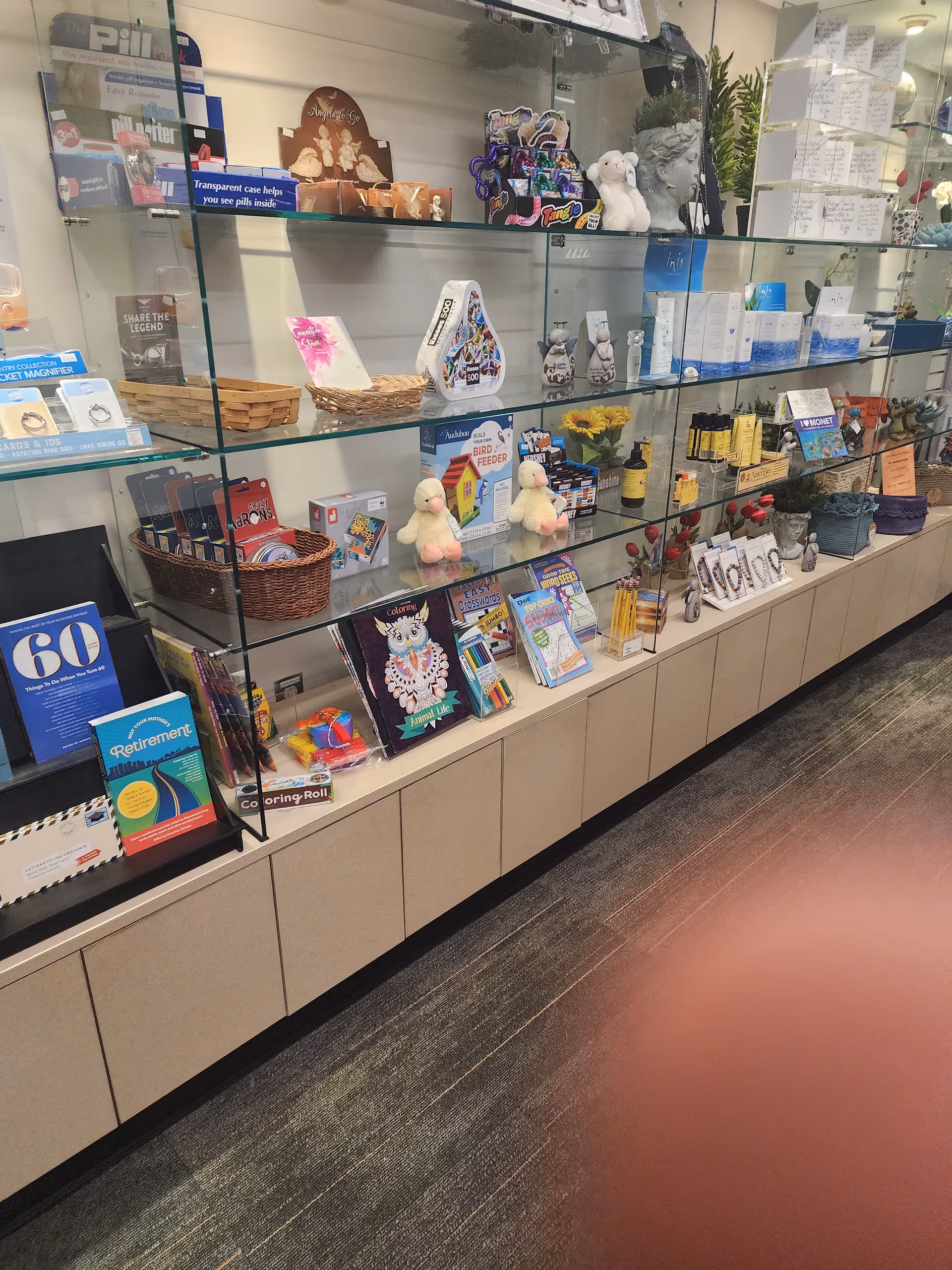 Glass display shelves stocked with gifts, magazines, and plush items inside a hospital gift shop.