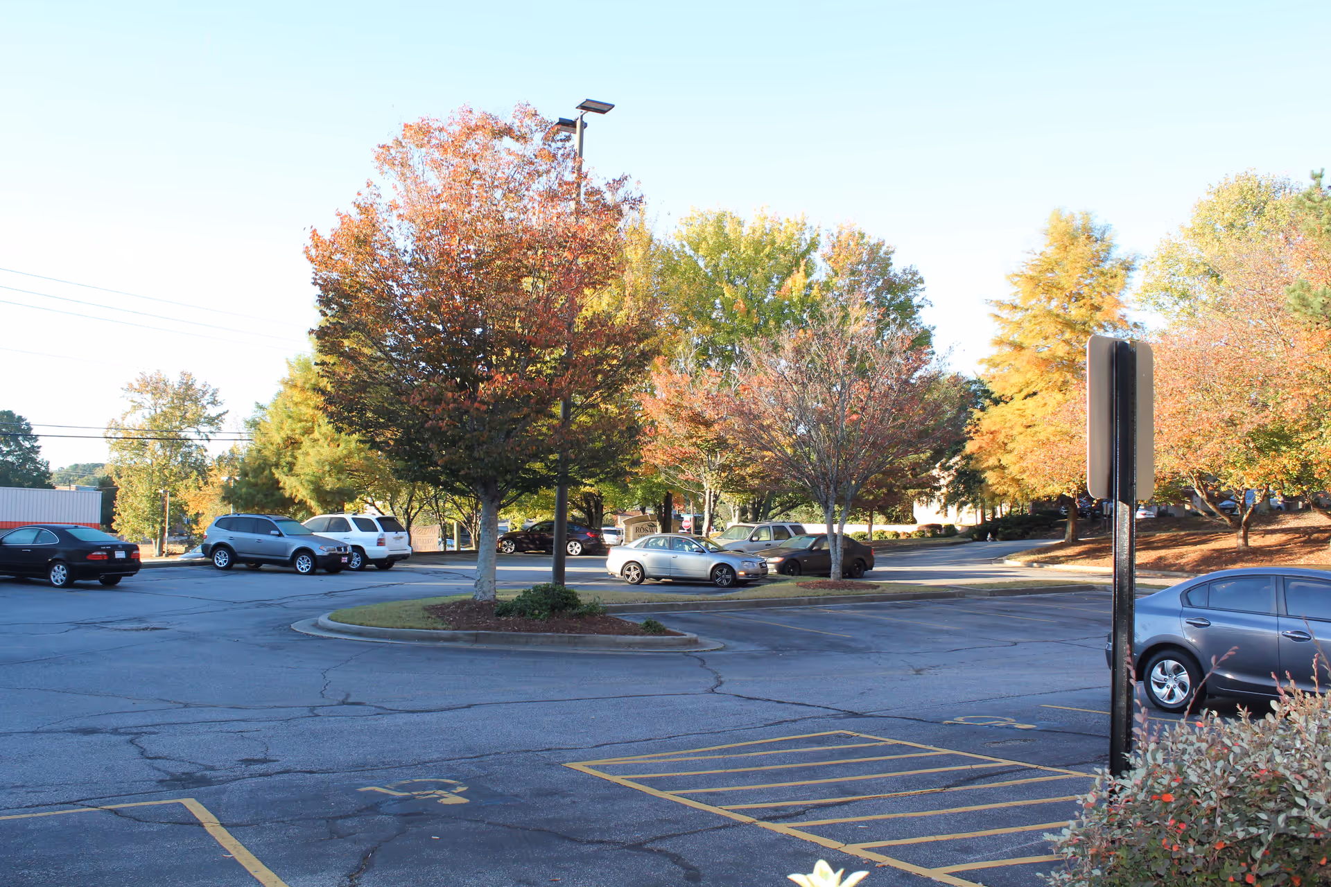 Outdoor parking lot with autumn trees and several parked cars near a facility.