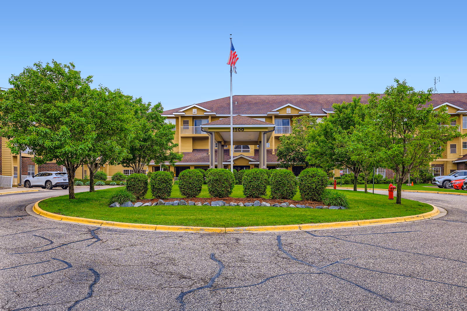 Exterior view of Tradition senior living facility with roundabout, greenery, and flag