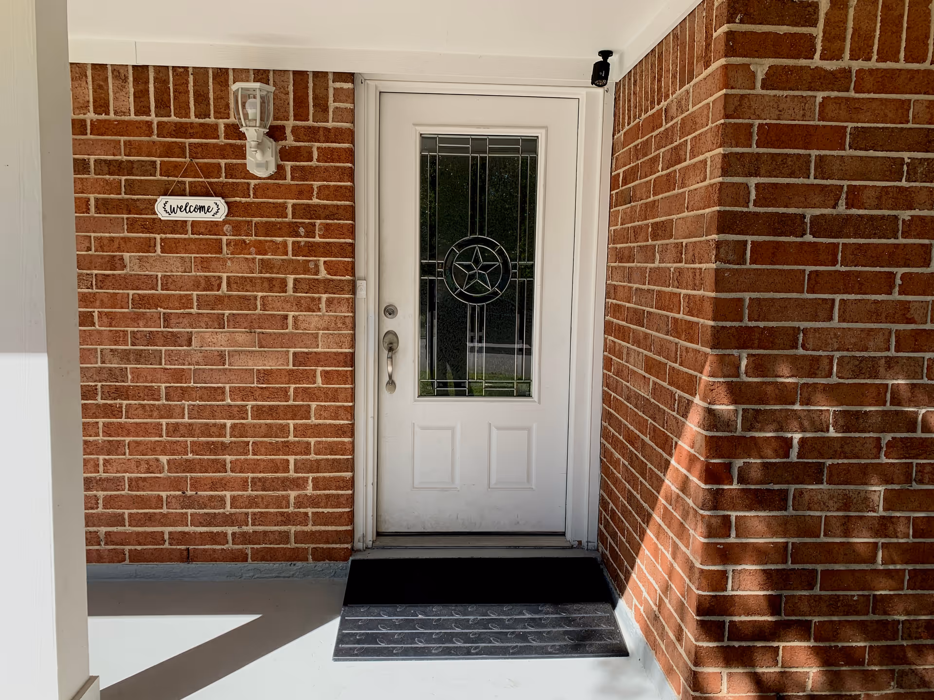 Brick exterior entrance with a white door, glass pane, and a small 'Welcome' sign.