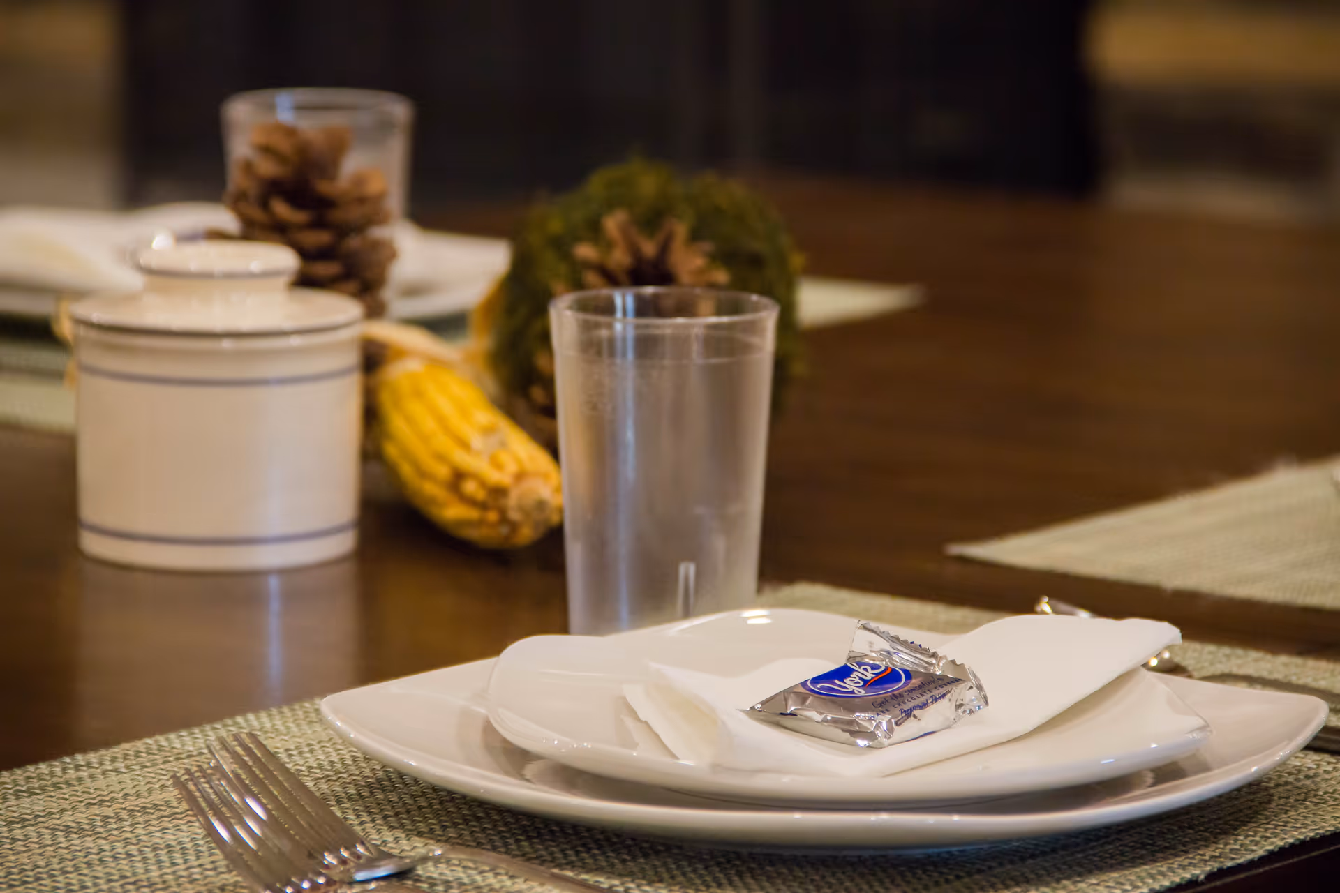 A dining table setup with plates, napkin, butter, and a glass.