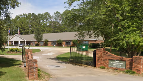 Gated entrance to Creekside Manor Assisted Living with brick pillars and a low building.