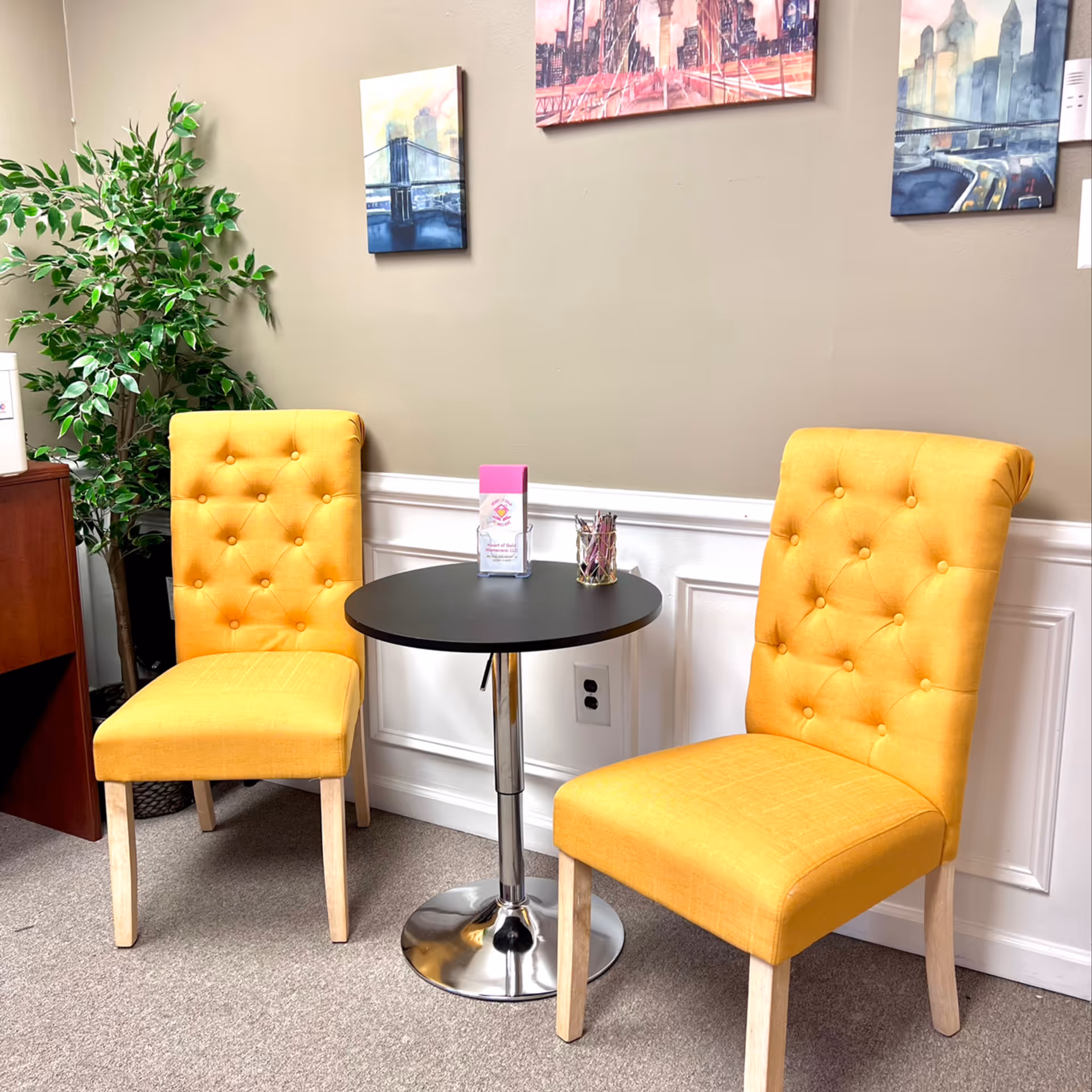 Two yellow tufted chairs surround a round black table in a cozy waiting area.
