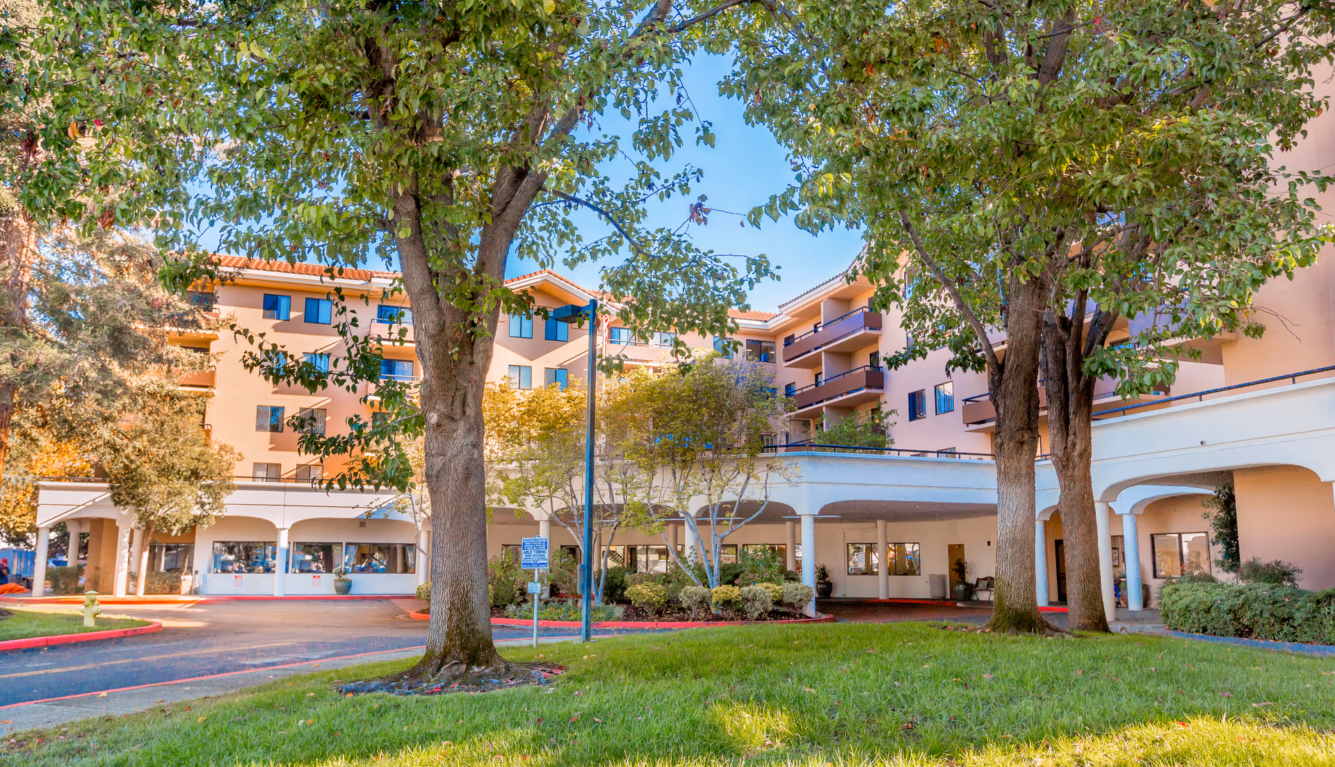 Exterior view of Brookdale Redwood City senior living campus with trees, arches, and a covered entrance.