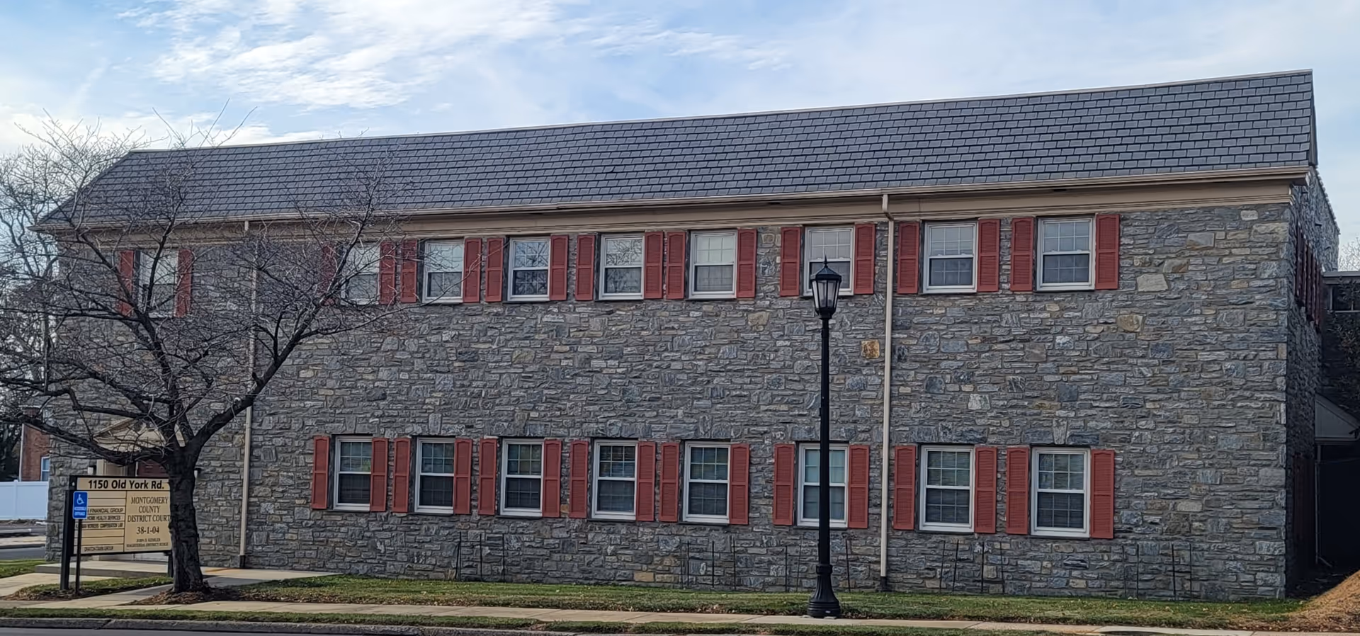 Two-story stone building with red shutters, a lamppost, and a sign on the sidewalk