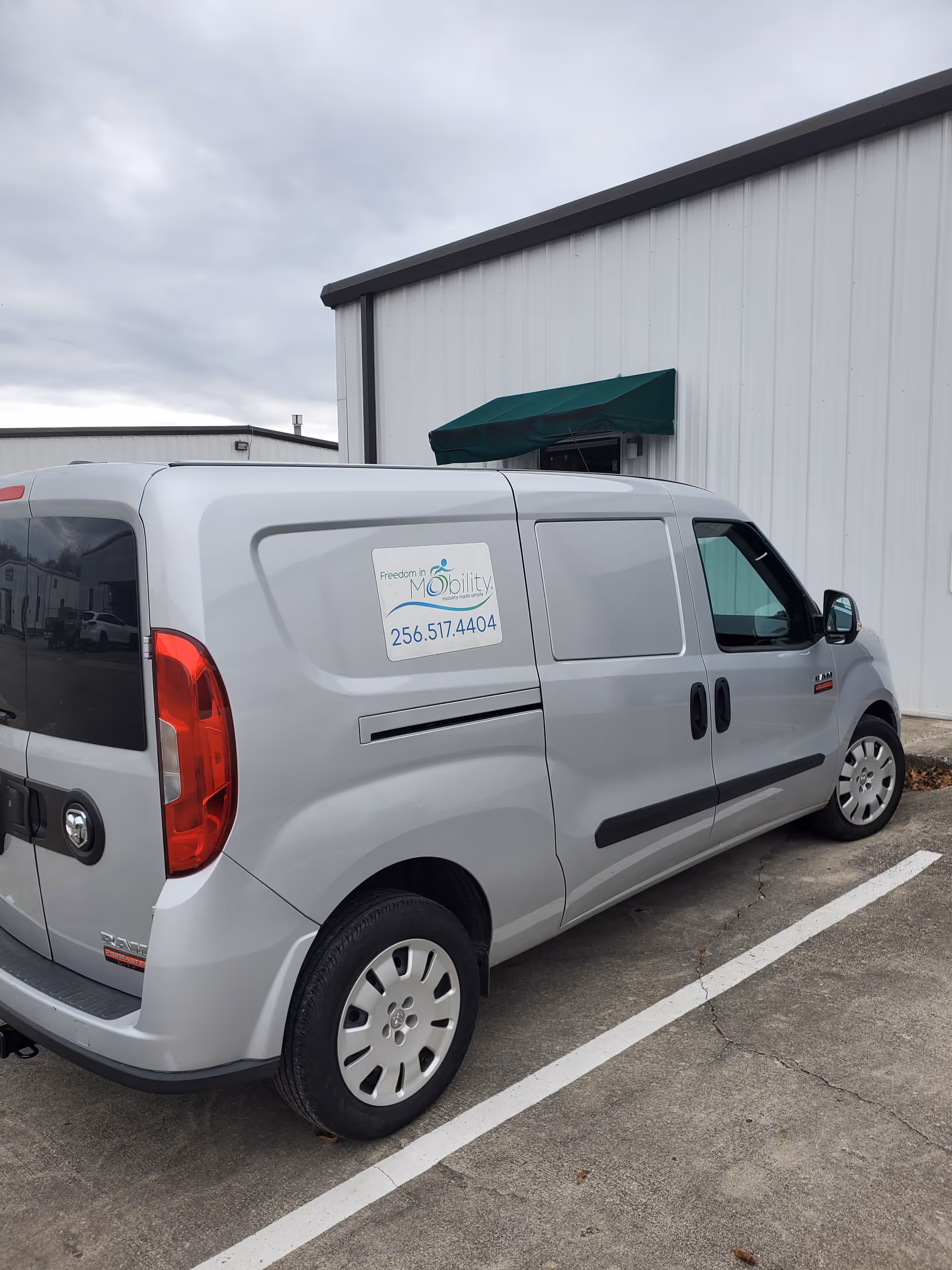 Silver mobility van with a Freedom In Mobility sticker sits beside a gray metal building.