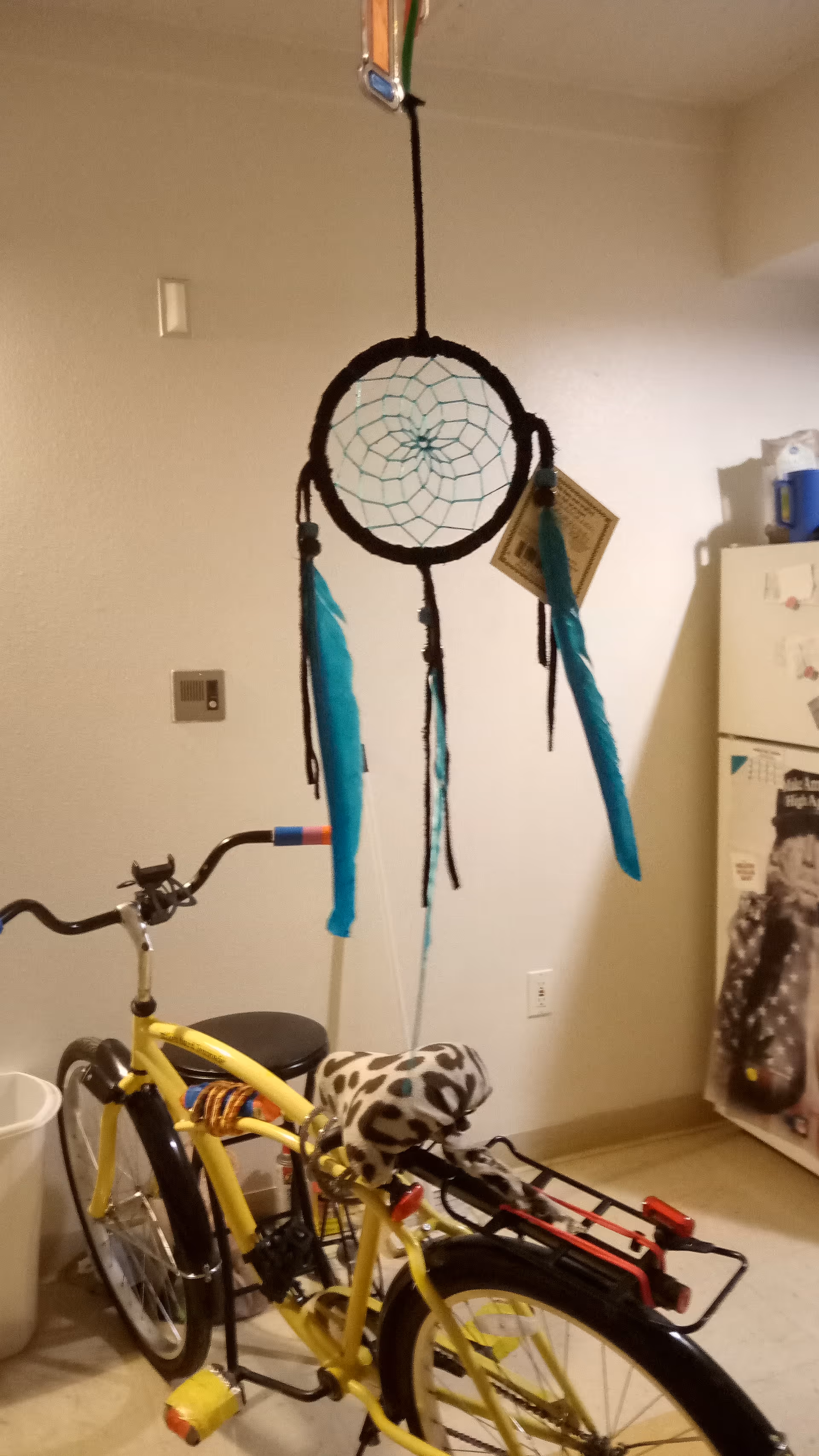 Interior utility room with a yellow bicycle, dreamcatcher, and refrigerator.