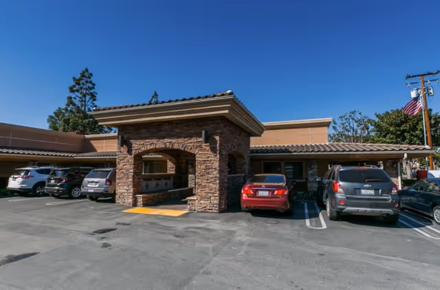 Stone-front entryway of a senior living facility with parked cars and blue sky.