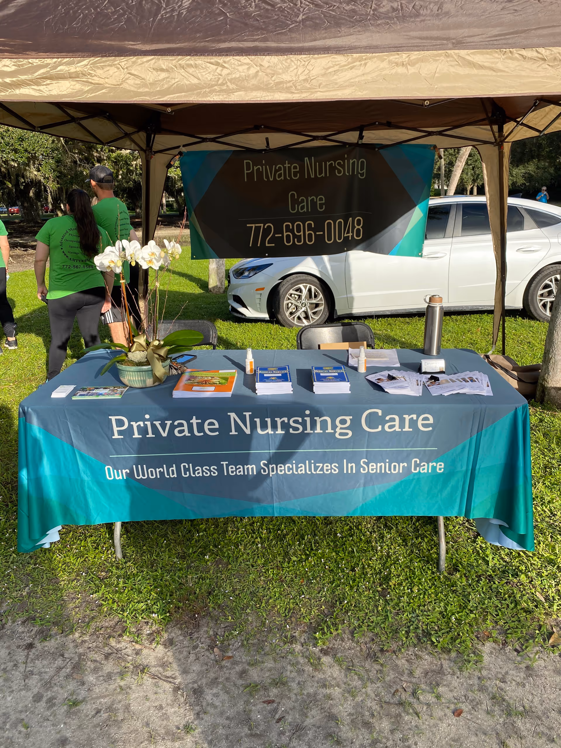 Outdoor canopy booth for Private Nursing Care with banner, brochures, and staff.