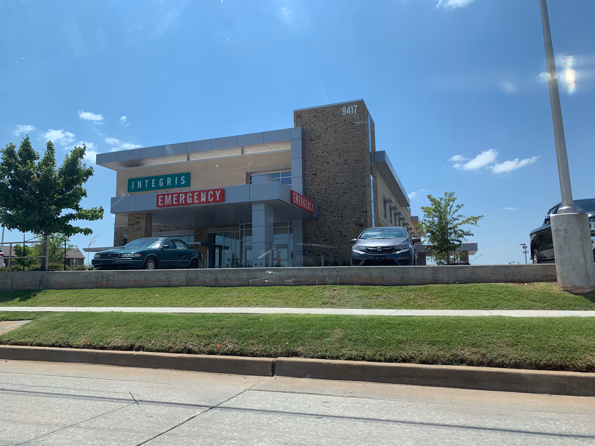Exterior view of INTEGRIS Health Community Hospital entrance with emergency signage and cars.