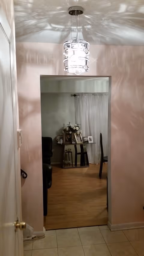 Pink-walled hallway leads to a living area with a small table, photos, and curtains.