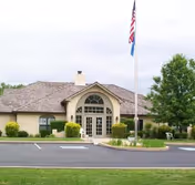 Single-story facility exterior with arched entrance, flagpoles, and surrounding parking.