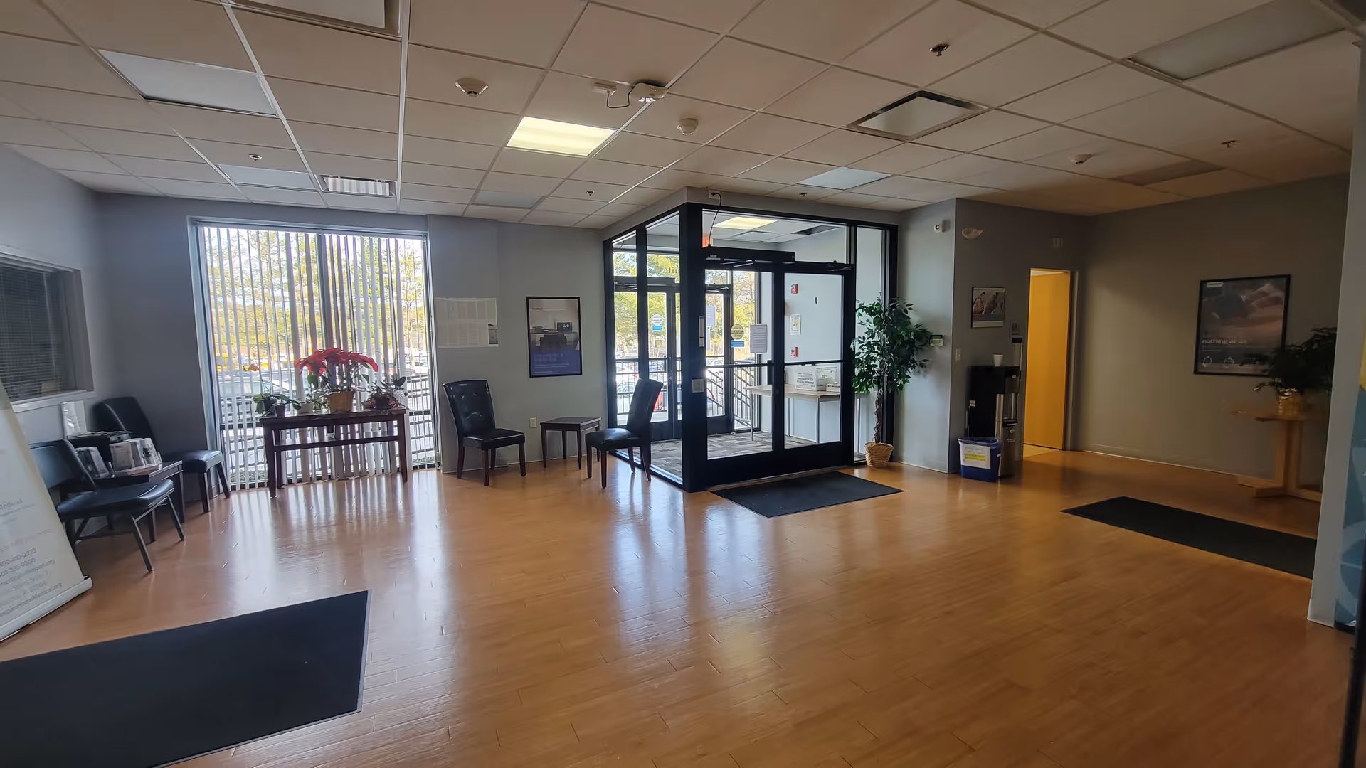 Senior living facility lobby with glass entrance doors, seating, plants, and wooden floor.