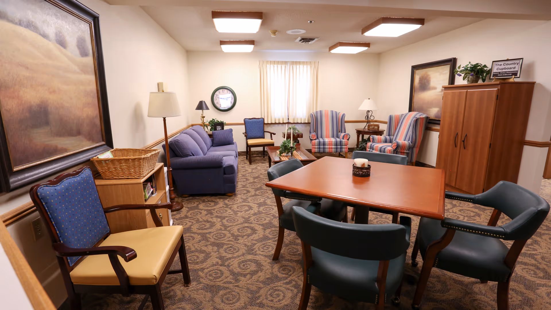 Interior senior living lounge with seating, tables, lamps, and artwork.
