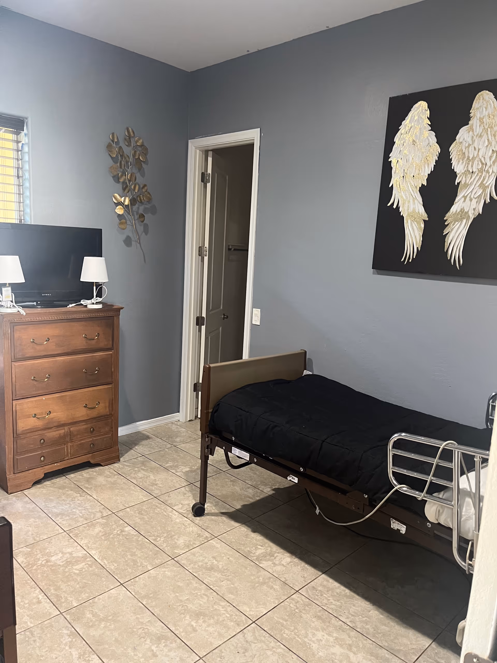 A small bedroom with a single bed, dresser, TV, and angel wings wall art.