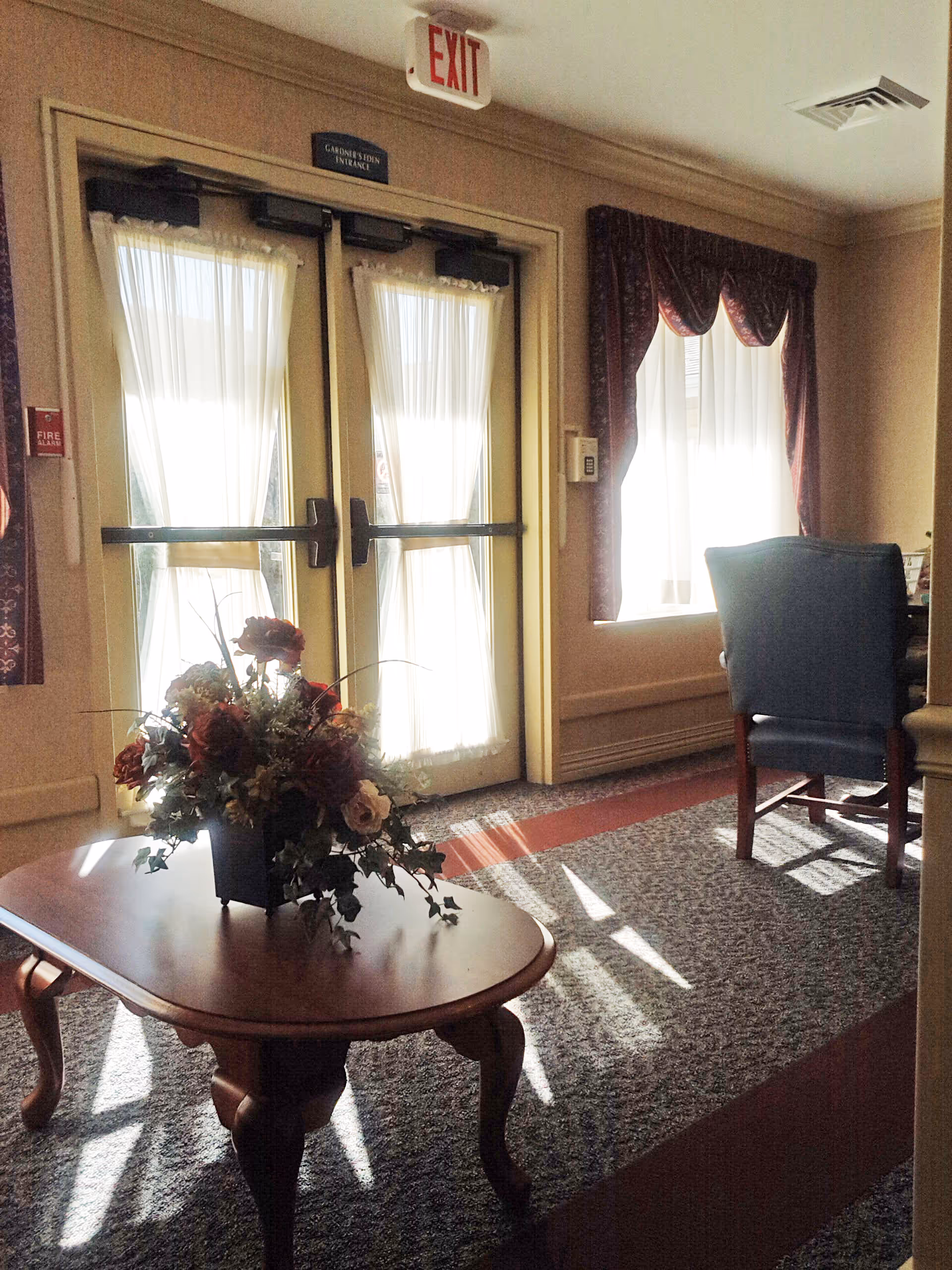 Interior lobby with double doors, sheer curtains, a round table, and a floral centerpiece.