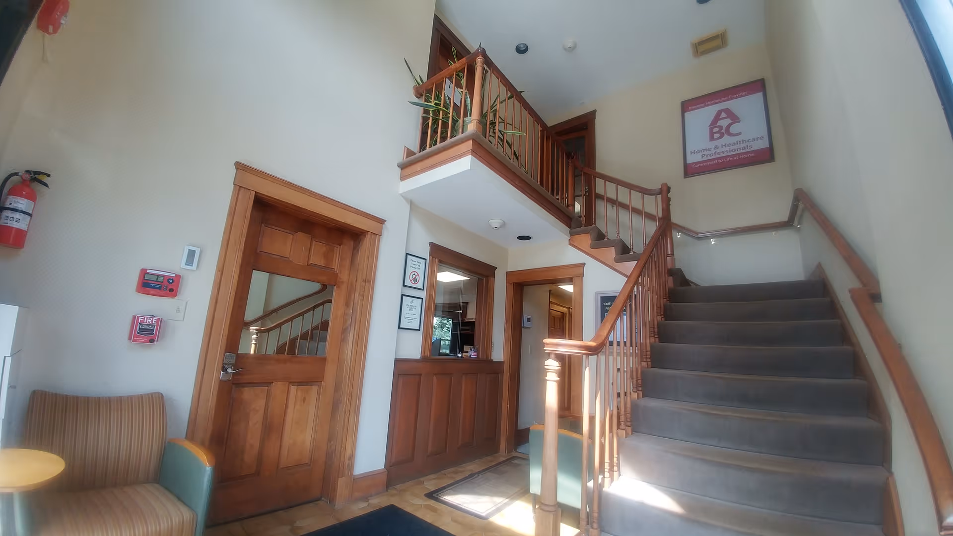 Two-story lobby with wooden staircase, reception desk, and seating in a senior facility.
