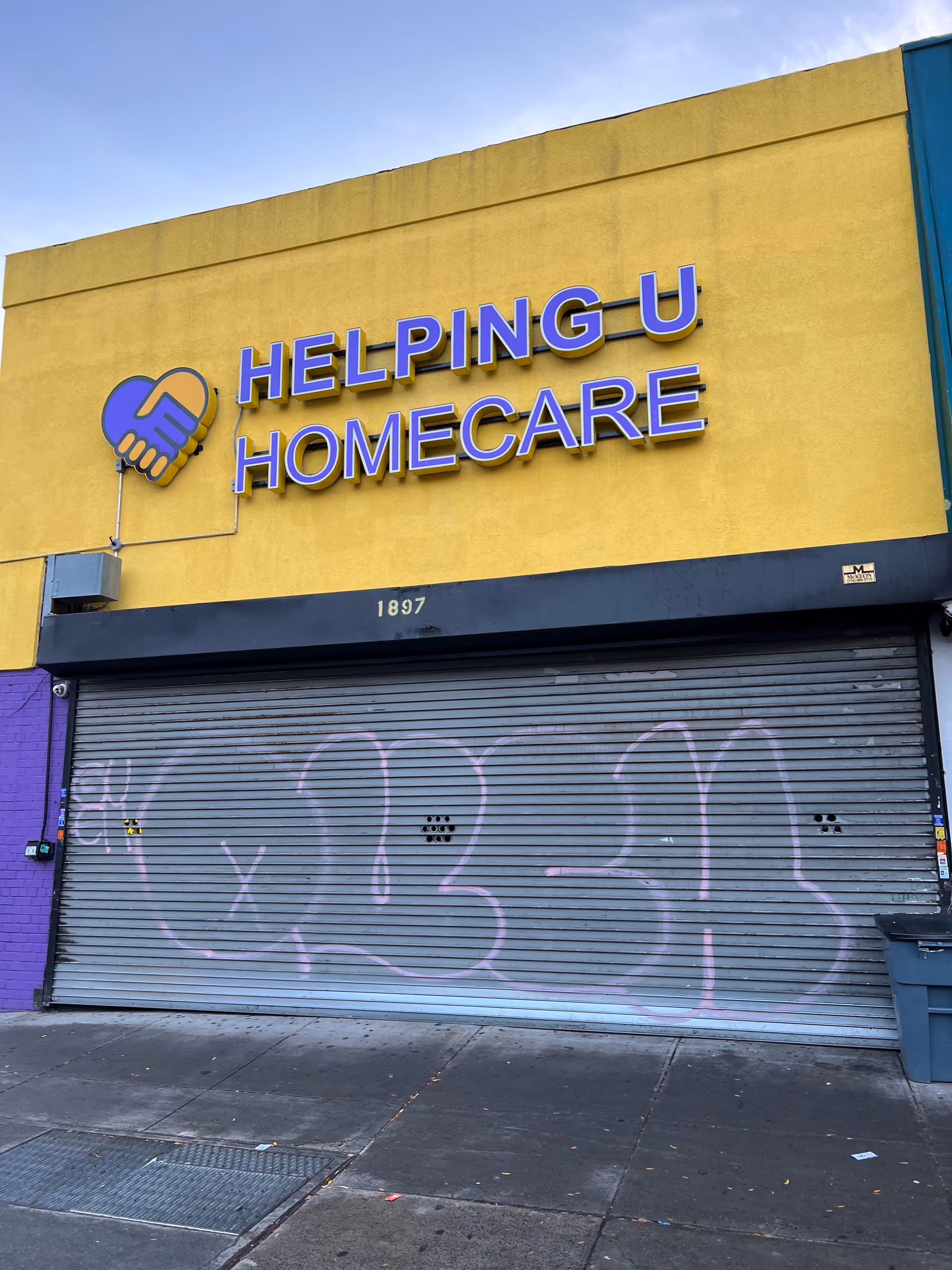 Yellow storefront with Helping U Homecare sign and graffiti-covered gray metal shutter.