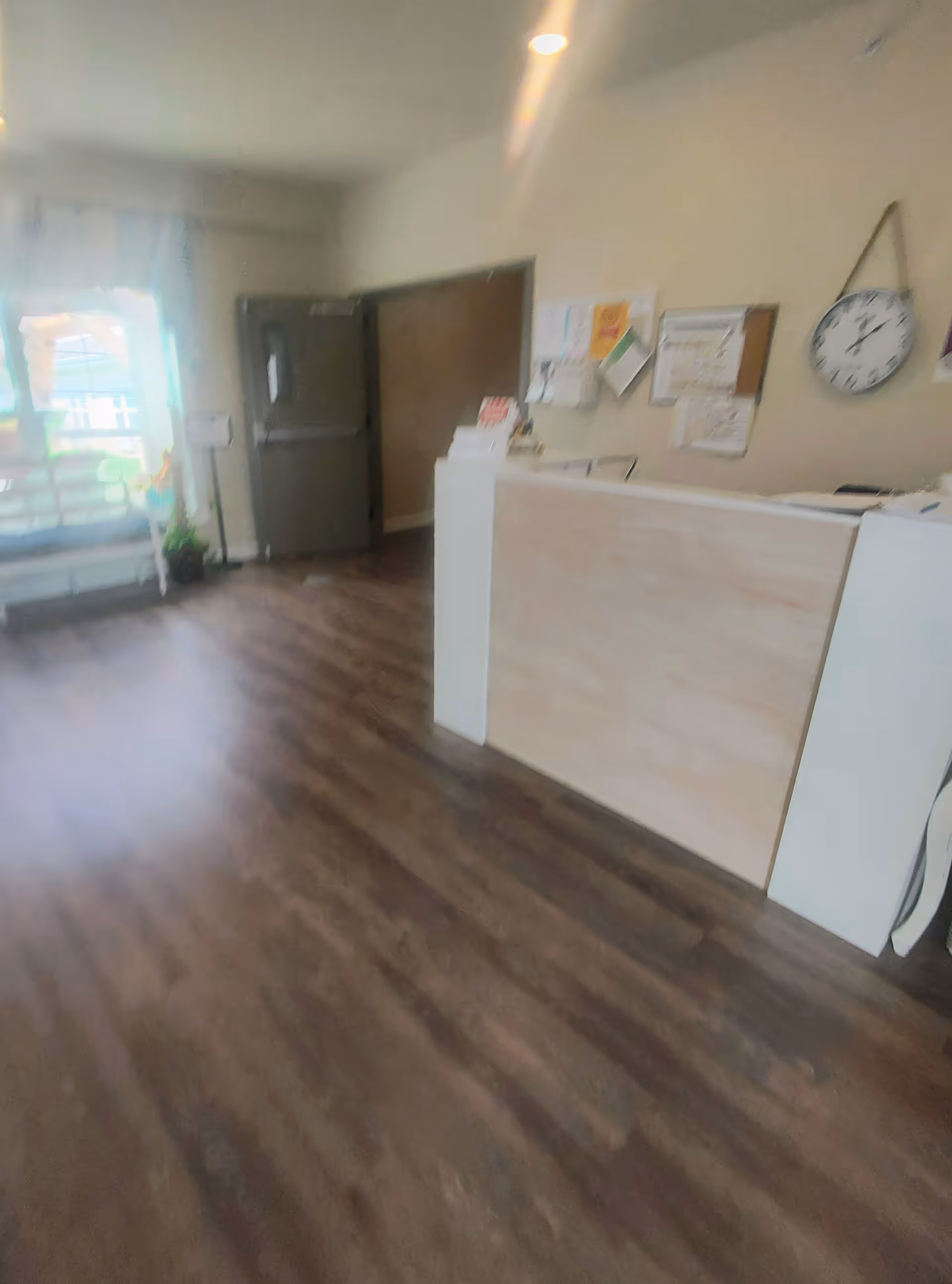 Reception desk in a bright, spacious lobby with bulletin board and clock.