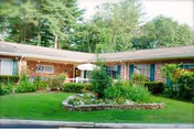 Exterior, single-story brick facility with manicured lawn, shrubs, and a Sudbury Pines Extended Care sign.