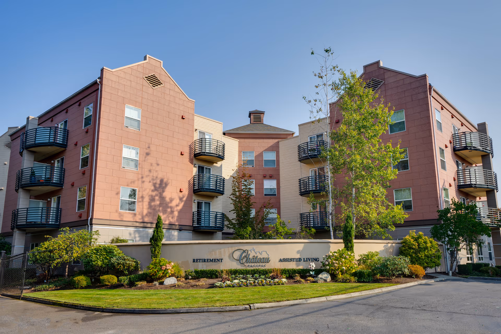 Front exterior of a four-story retirement/assisted living building with balconies, landscaping, and a sign reading 'Chateau'.