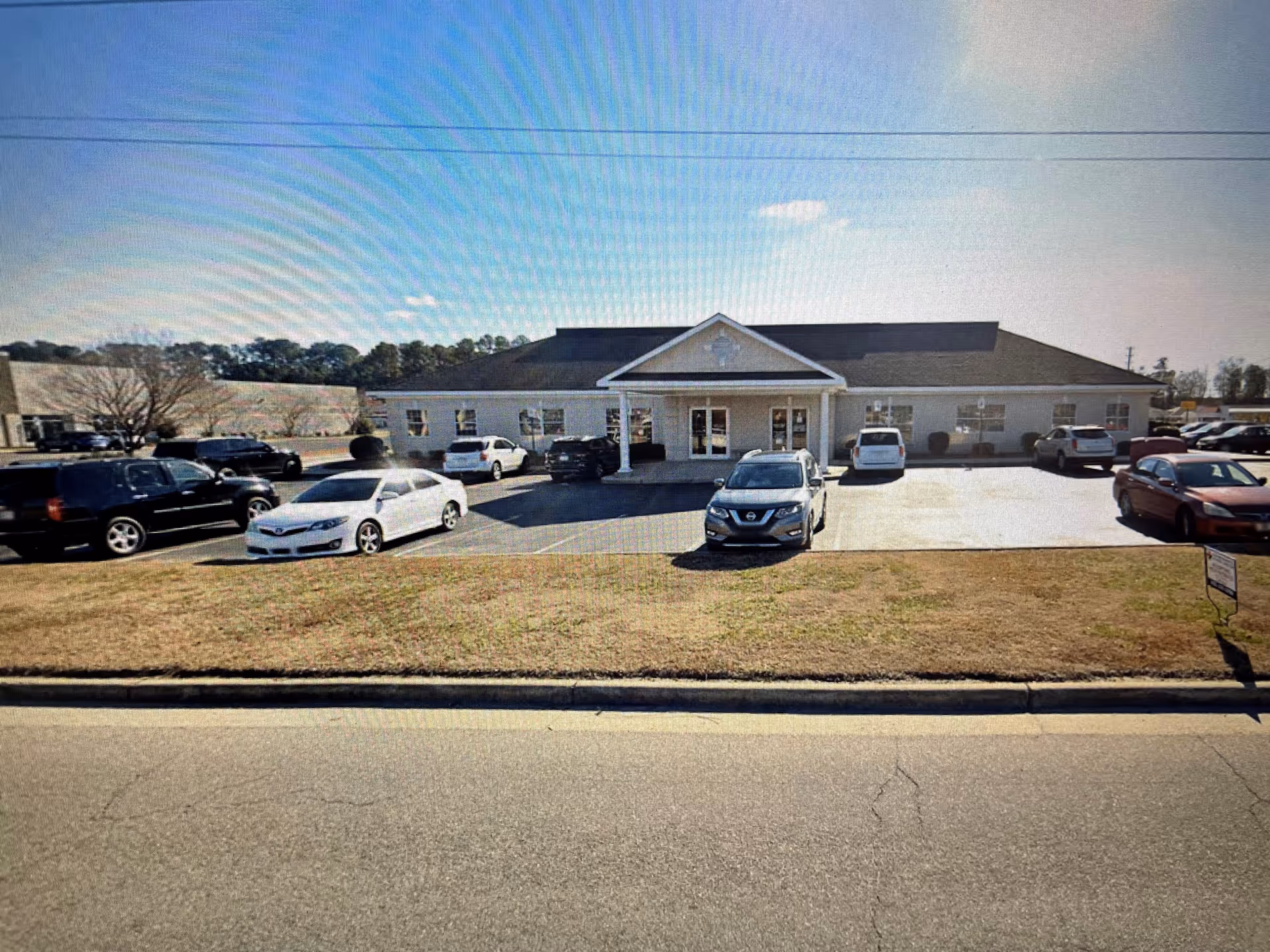 Single-story hospice facility with a front entrance and numerous parked cars.