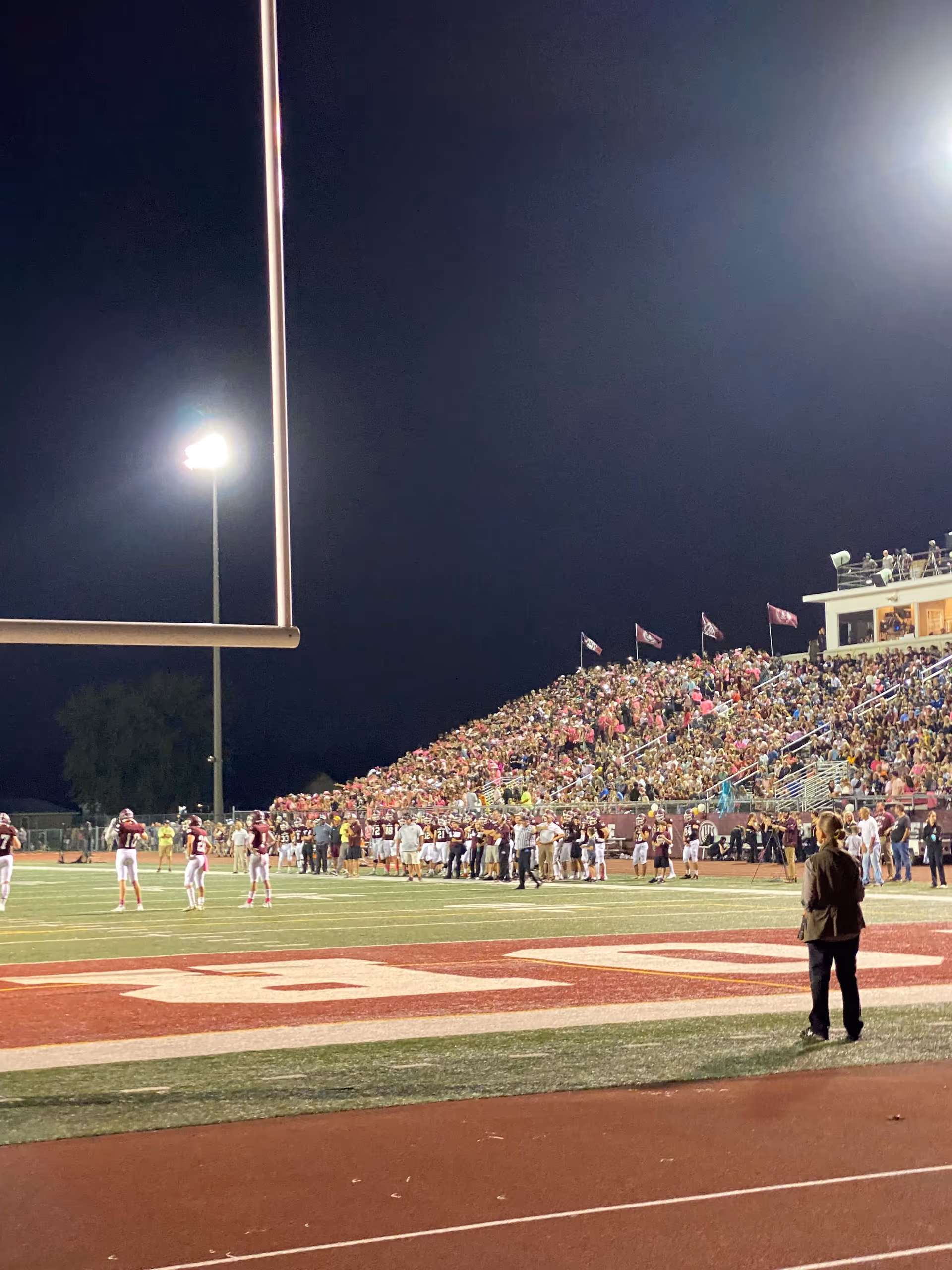 Nighttime football stadium scene with a large crowd in the bleachers and players on field.