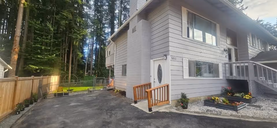 Two-story gray elder care home exterior with stairs, driveway, and landscaped front yard.