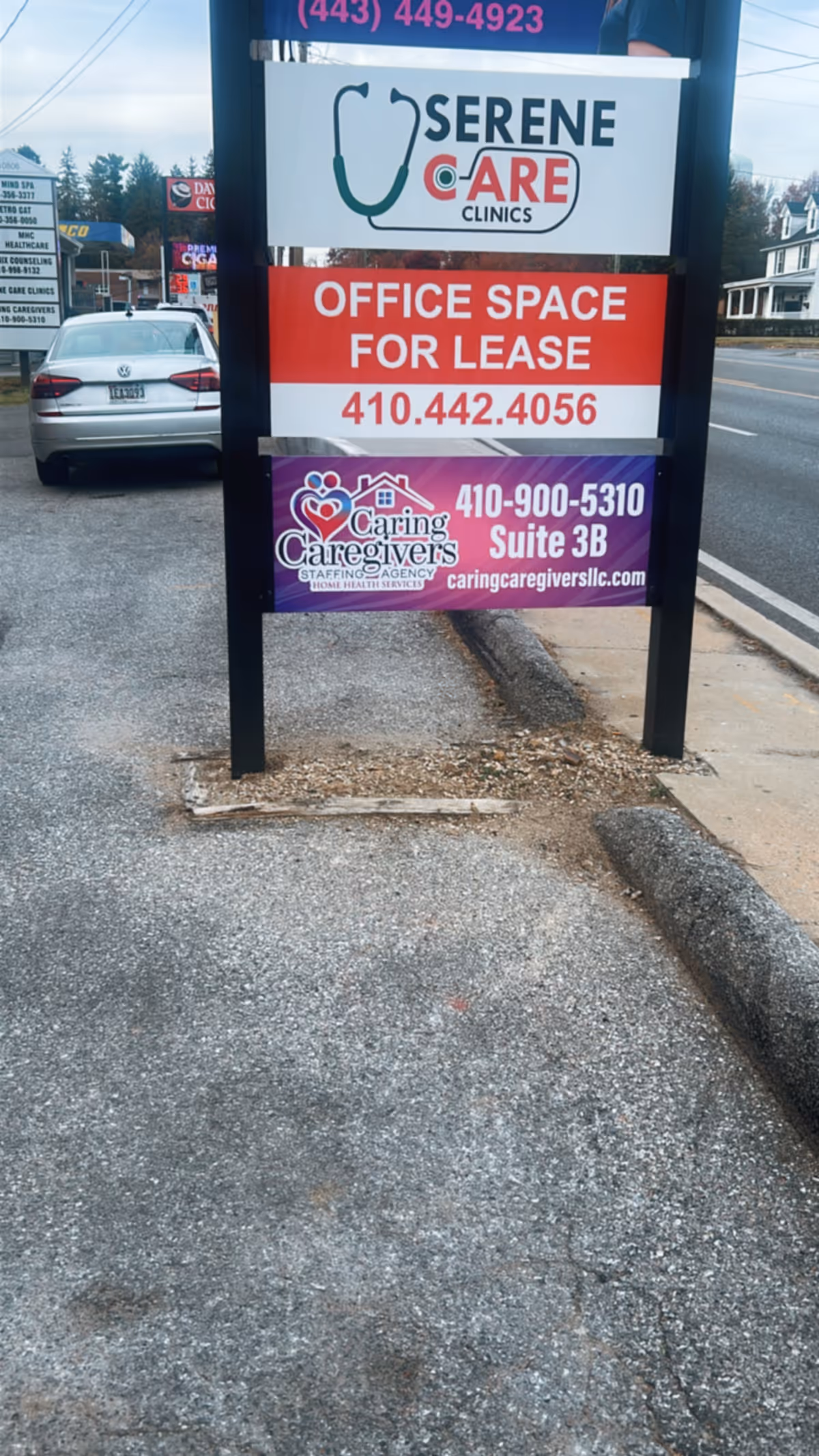Exterior signpost along sidewalk showing Serene Care Clinics, office lease, and Caring Caregivers ads.