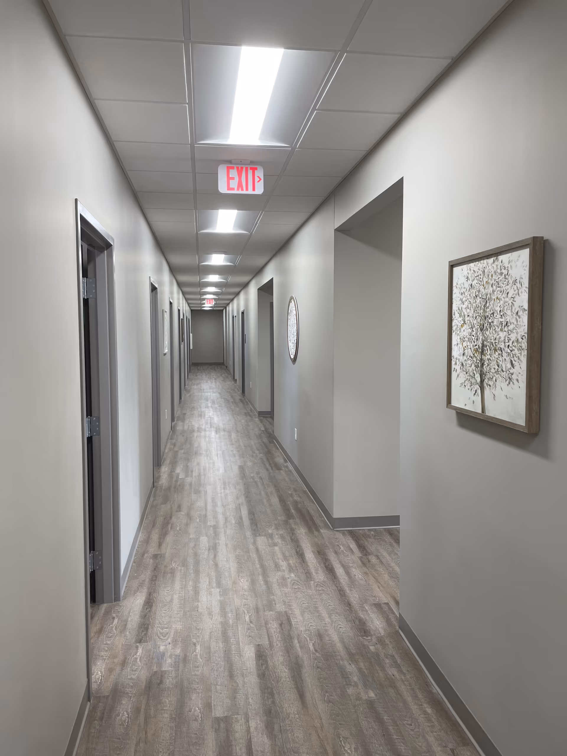 Long gray interior hallway in a senior living facility with multiple doors and an EXIT sign.