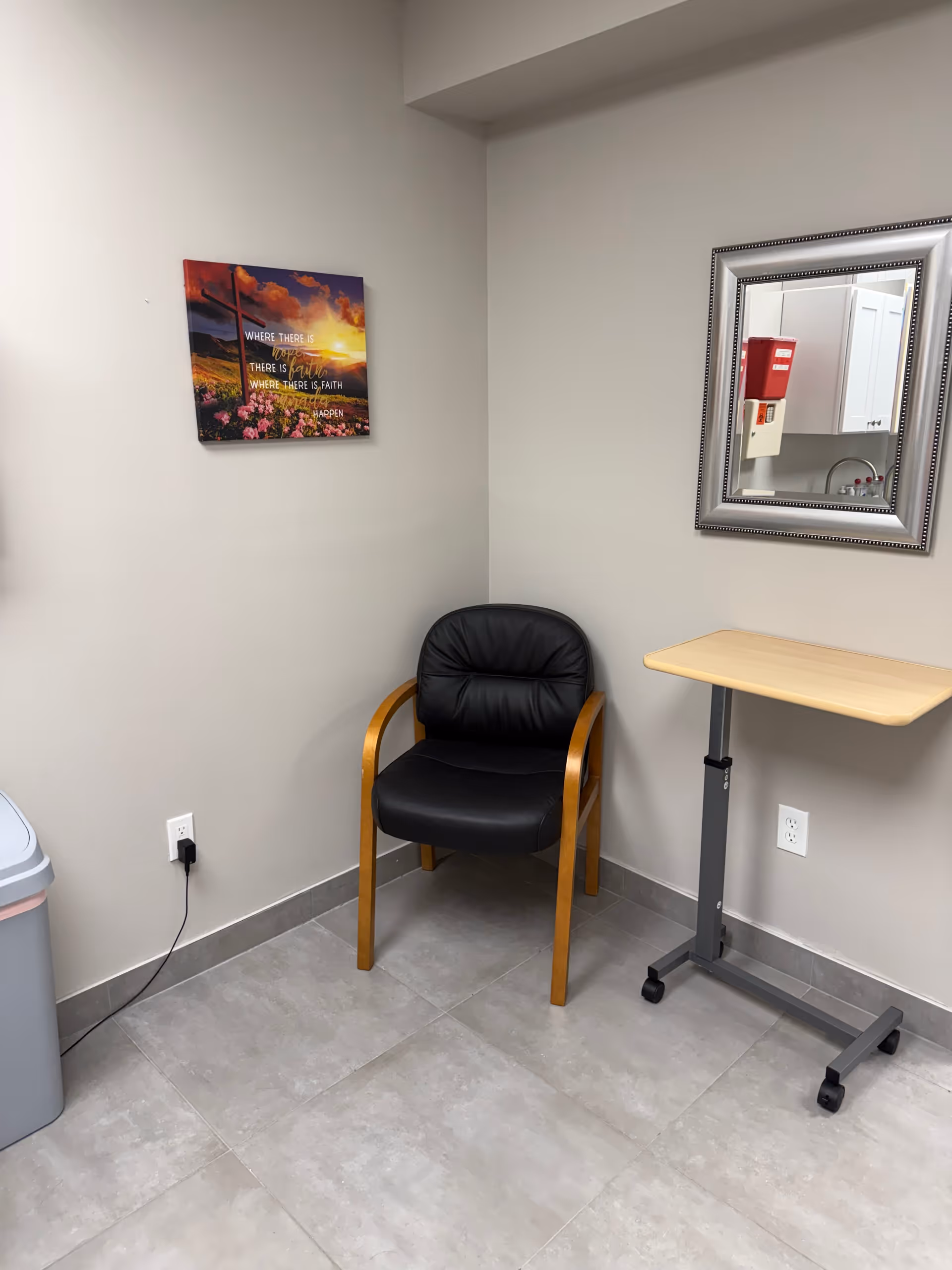 A small neutral corner with a black chair, rolling table, wall art, and mirror.
