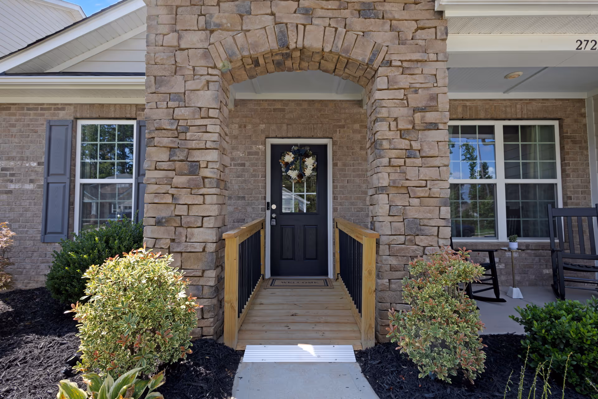 Stone archway entrance with wooden ramp leads to a dark front door decorated with a wreath