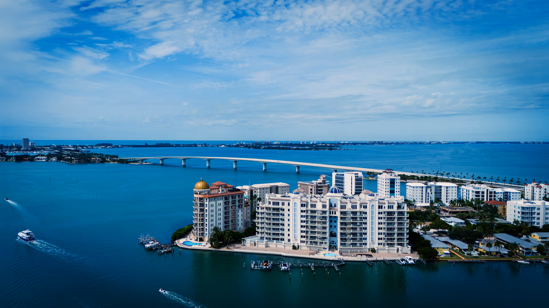 Aerial view of a coastal residential complex with a bridge over turquoise water.