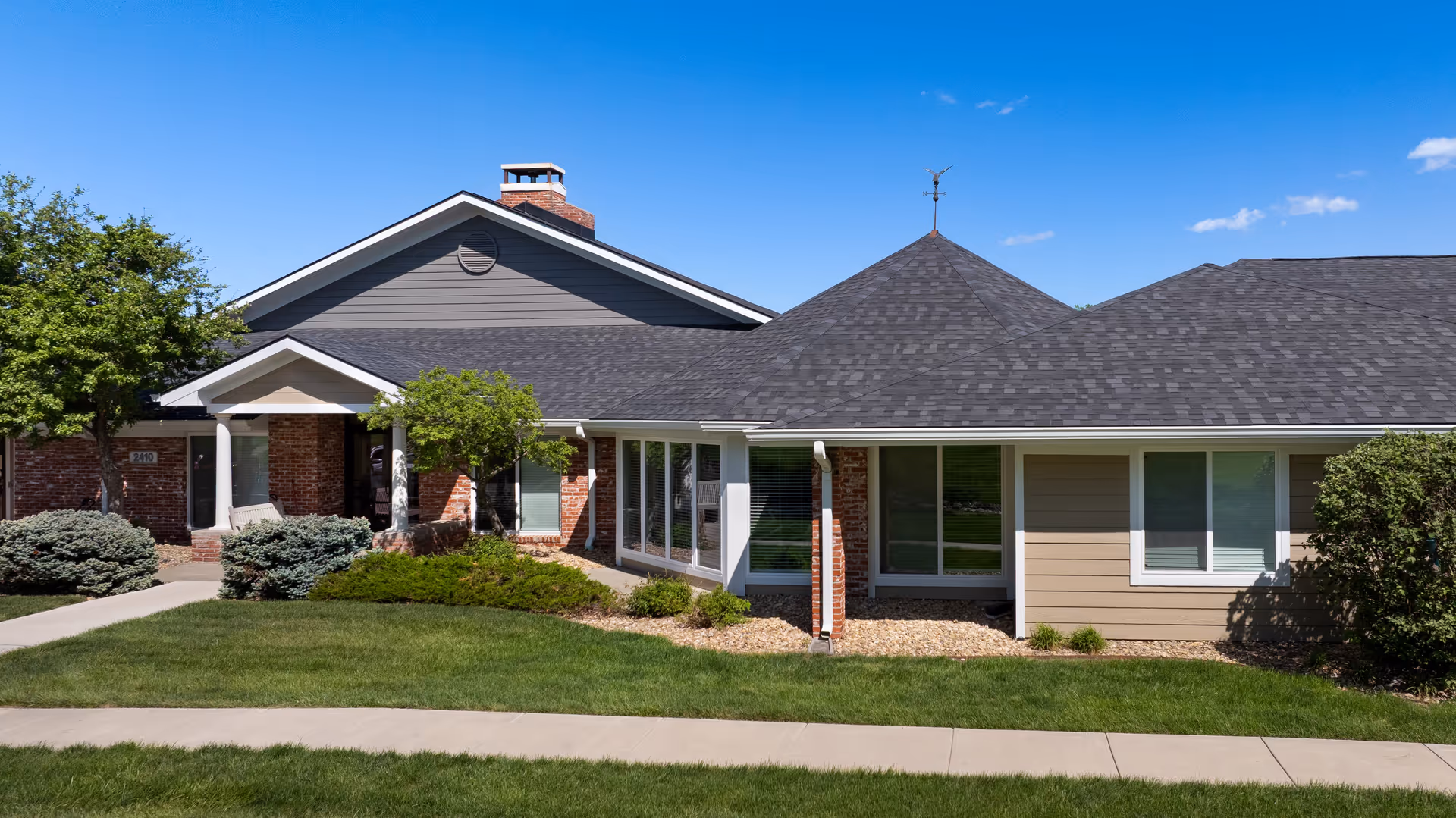 A single-story assisted living facility exterior with brick, siding, landscaped lawn and entrance.