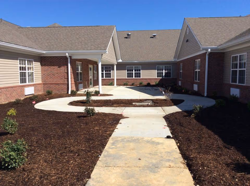 Courtyard with a paved walkway leading to the entrance of single-story brick-and-siding buildings under a clear blue sky.