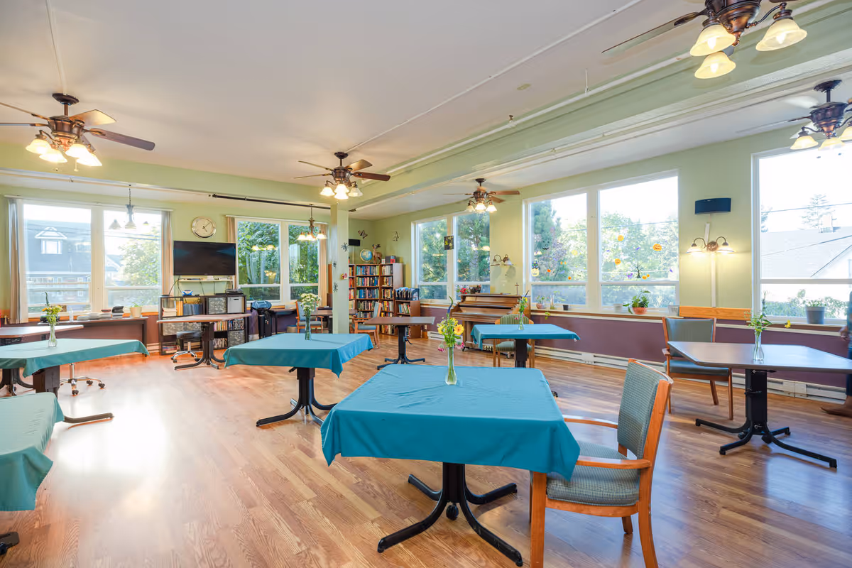 Bright, spacious interior common area with teal-covered tables, chairs, and large windows.