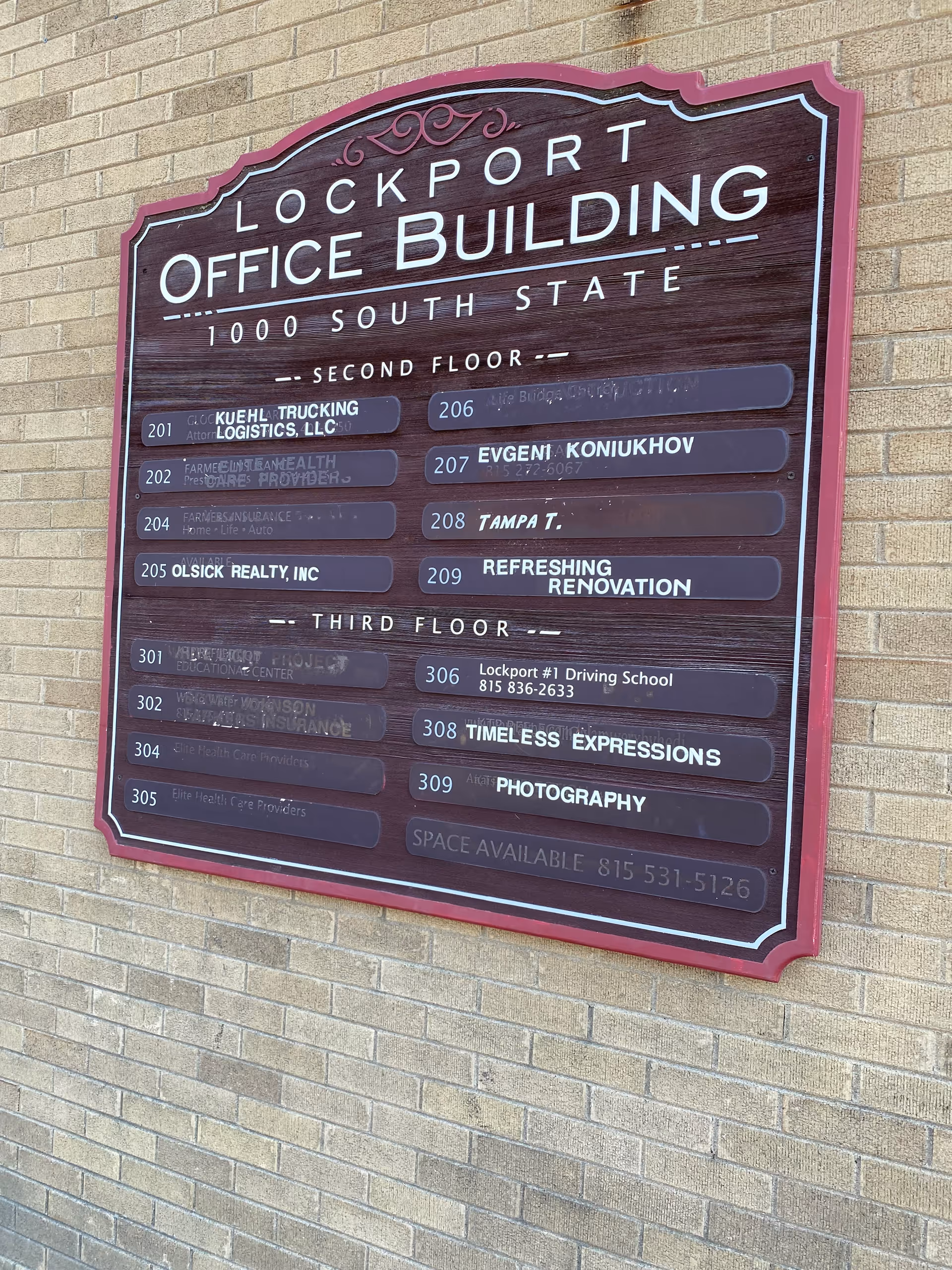 Large wooden directory sign on a brick wall listing offices on multiple floors.