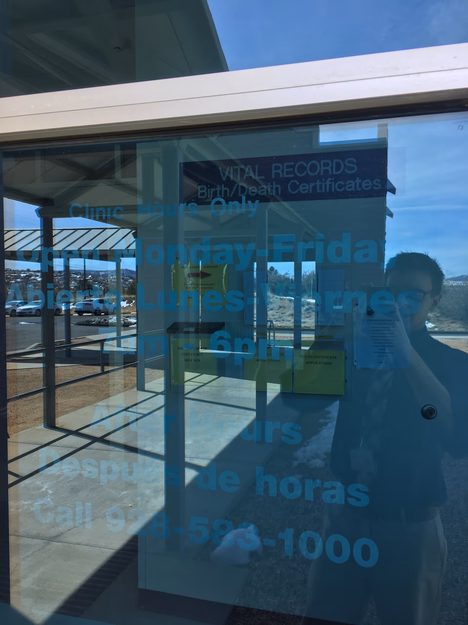 Glass door with blue clinic hours text, reflection of the photographer in the window.