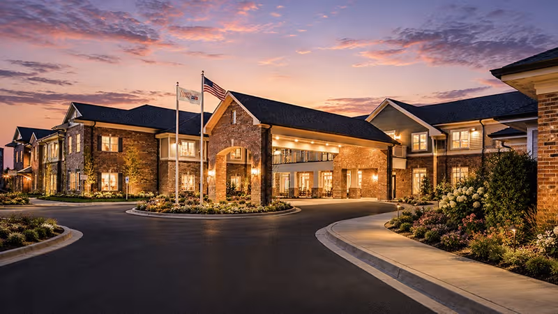 Sunset view of American House Mount Prospect exterior with brick facade and illuminated entrance.