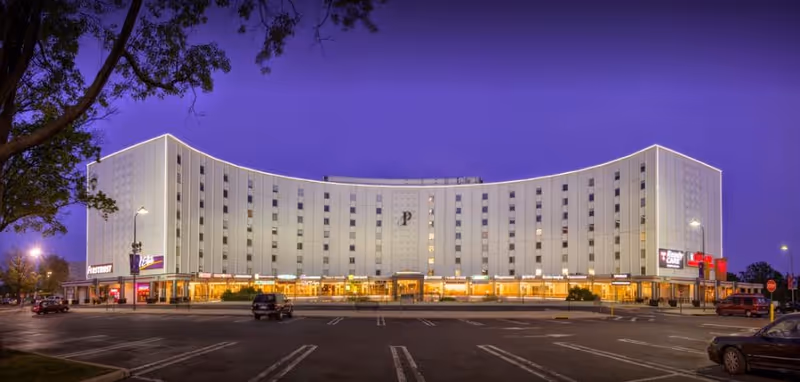 Exterior night view of a curved, white senior living building with illuminated storefronts.