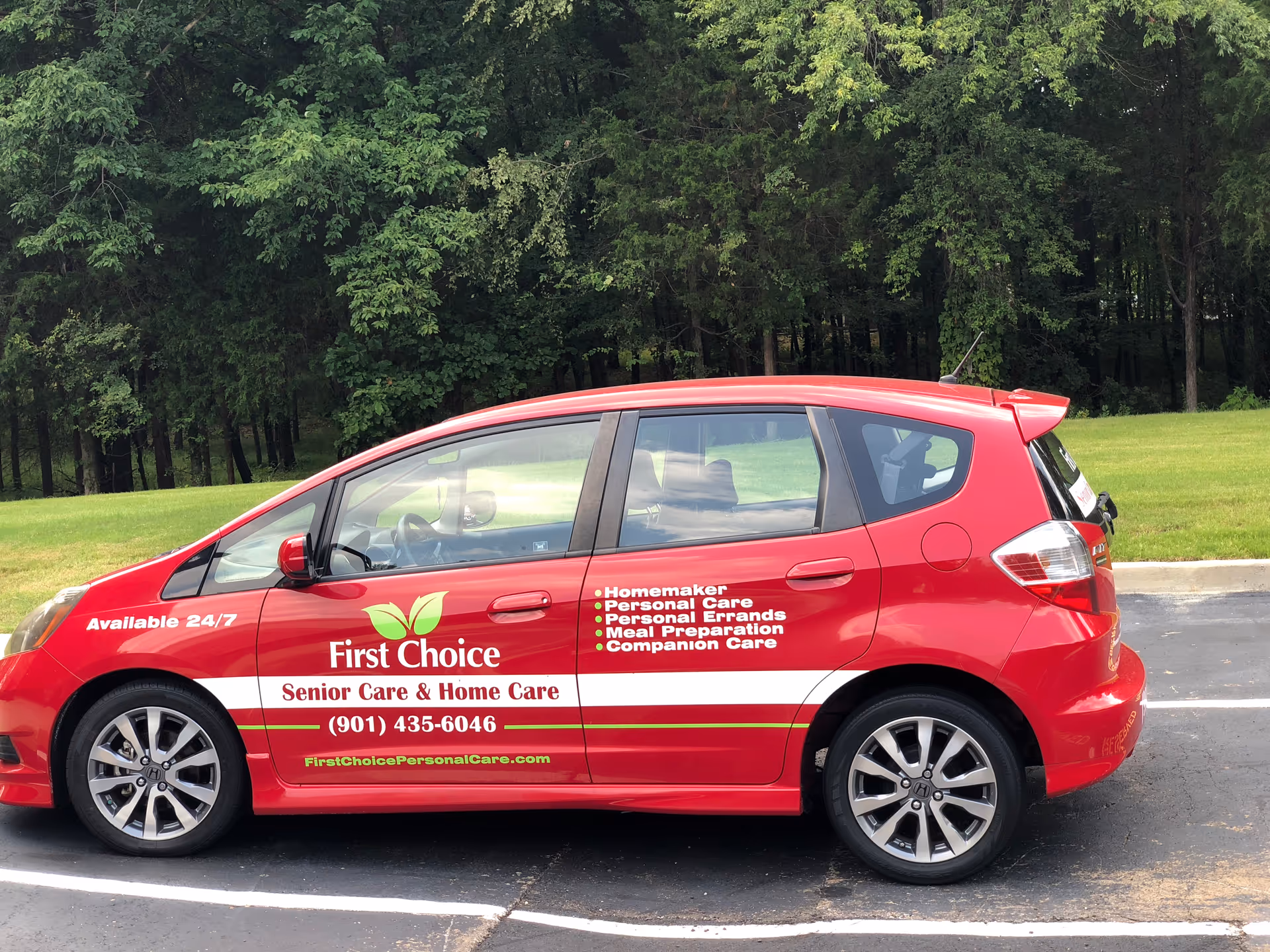 Red First Choice senior care vehicle parked in a lot with green trees behind.