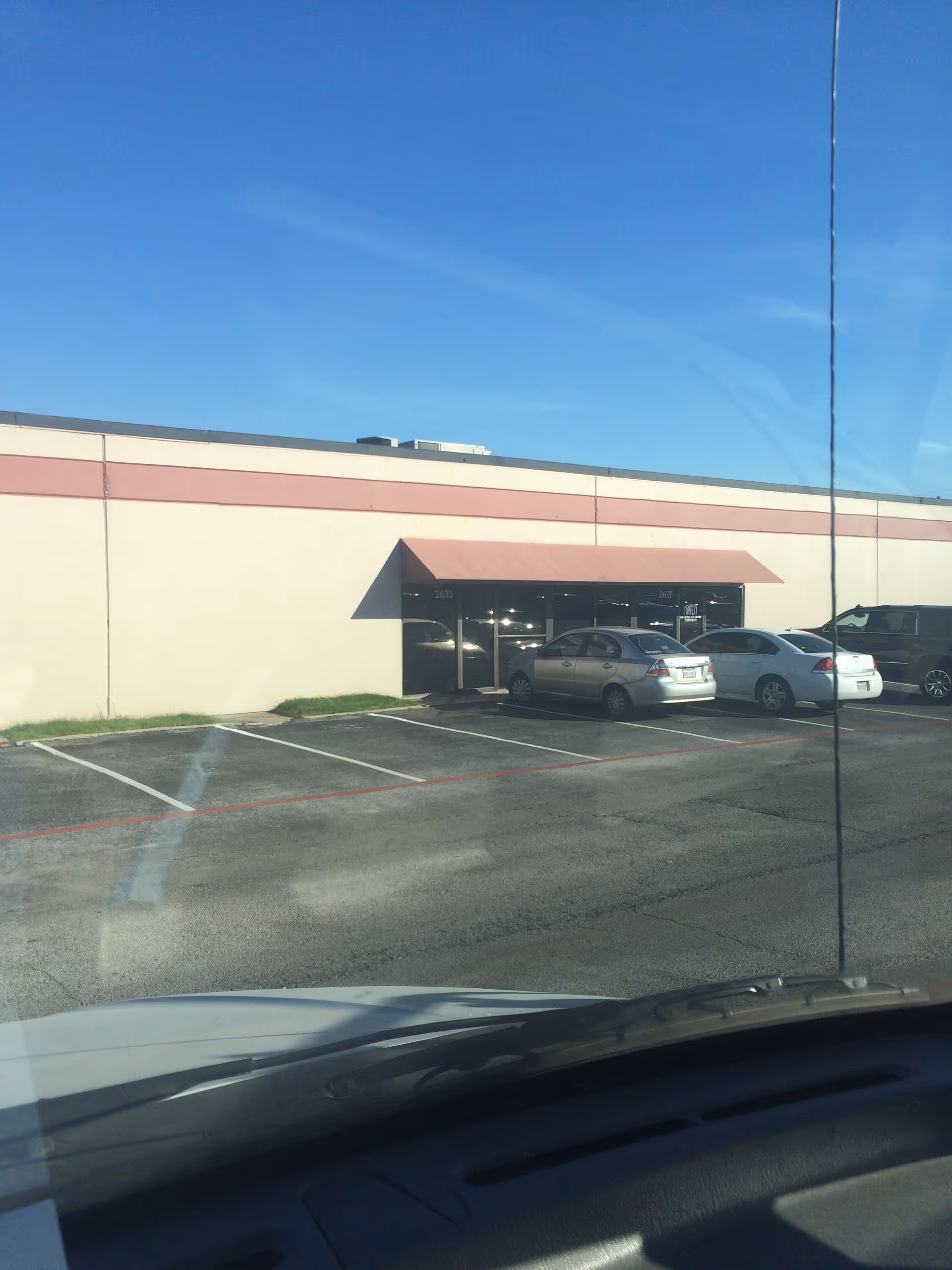Beige commercial building with maroon awning and parked cars in front.