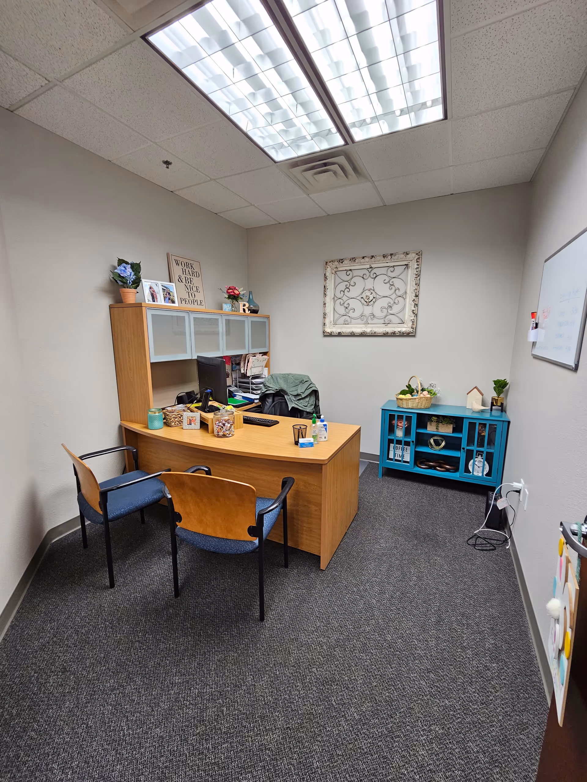 Small office with desk, computer, two chairs, and a decorative cabinet inside.